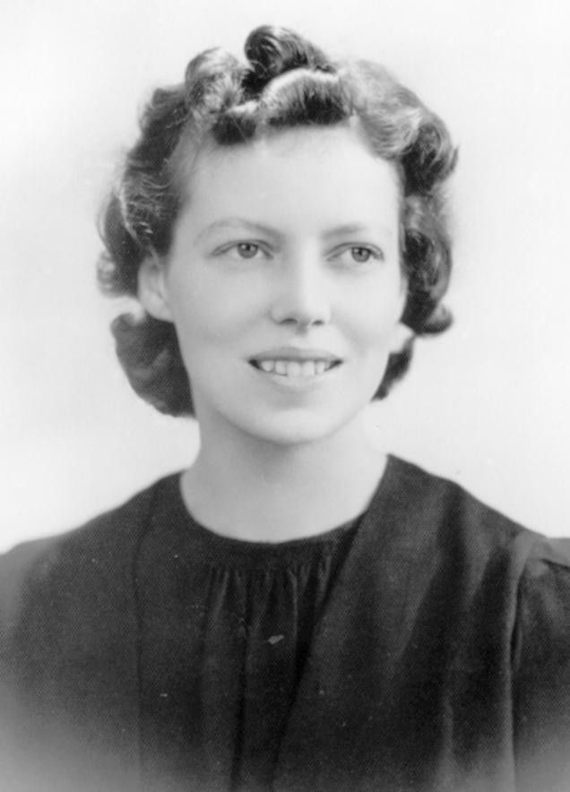 Black-and-white studio portrait of a smiling person with curled hair wearing a dark blouse