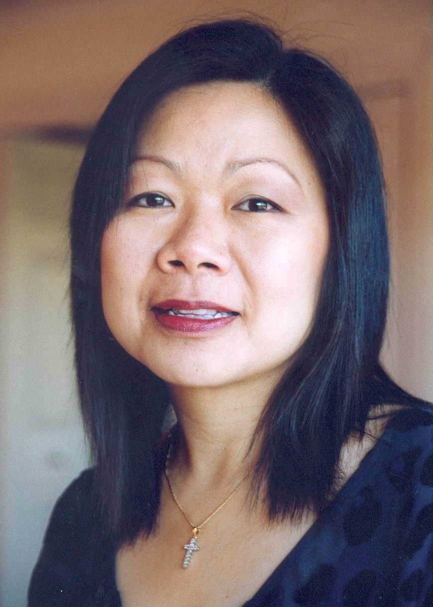 Portrait of a smiling person with shoulder-length dark hair wearing a black top and a cross necklace