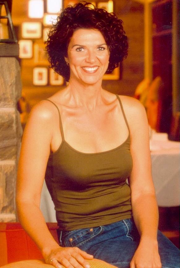 Smiling woman in a green tank top and jeans sitting indoors against a warm-toned background