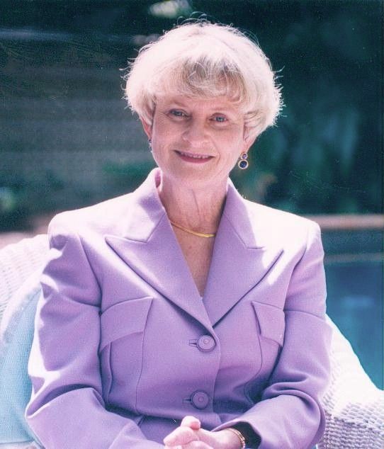 Woman in a lavender suit seated outdoors, smiling at the camera.
