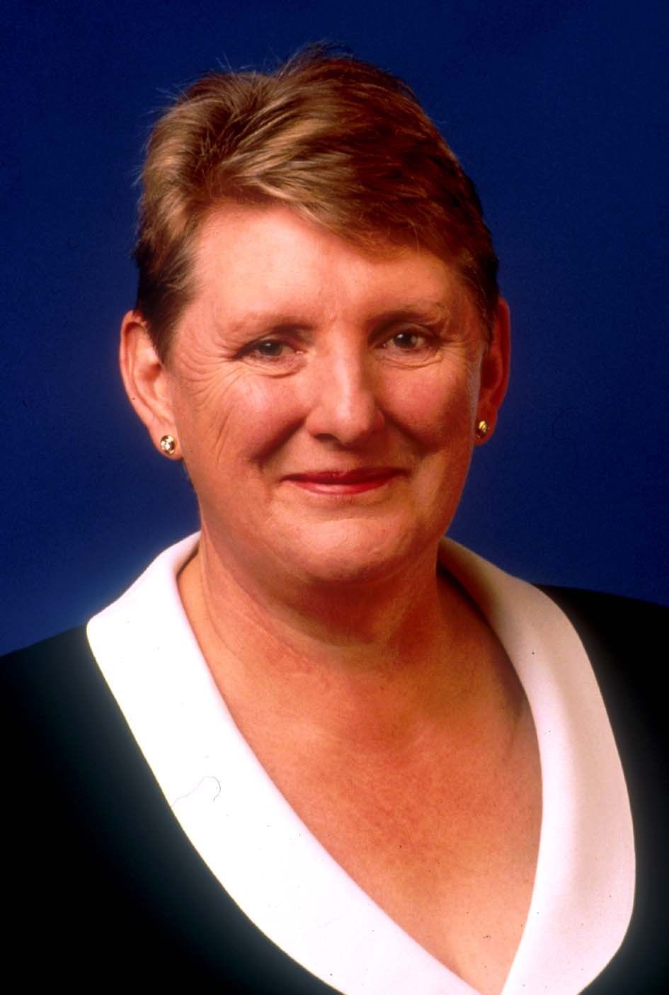 Portrait of a smiling woman in a black top with a white collar on a blue background