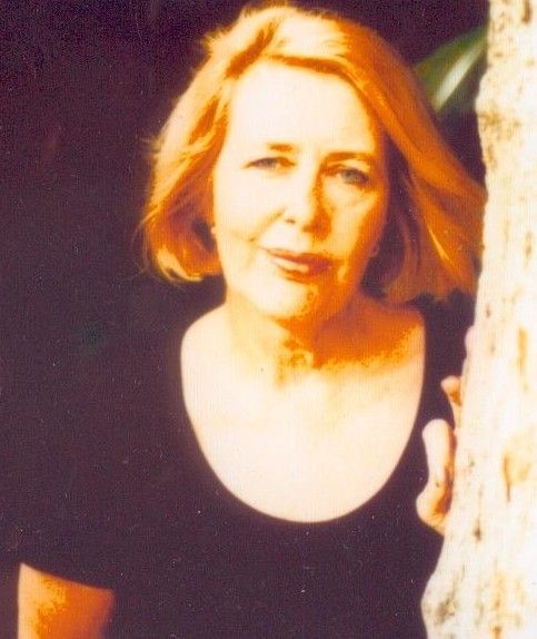 Woman in a black top standing beside a tree, with a slight smile and warm lighting.