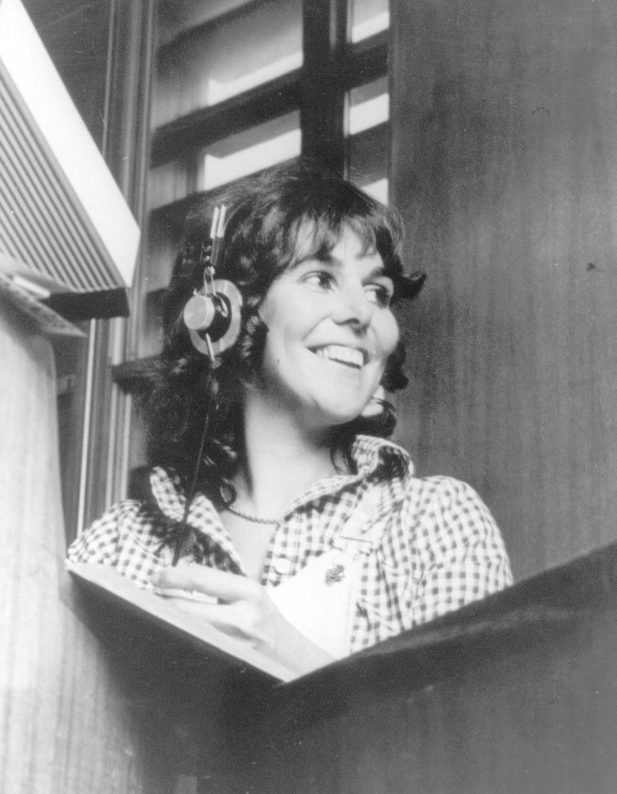 Woman wearing headphones and smiling at a radio microphone in a studio booth