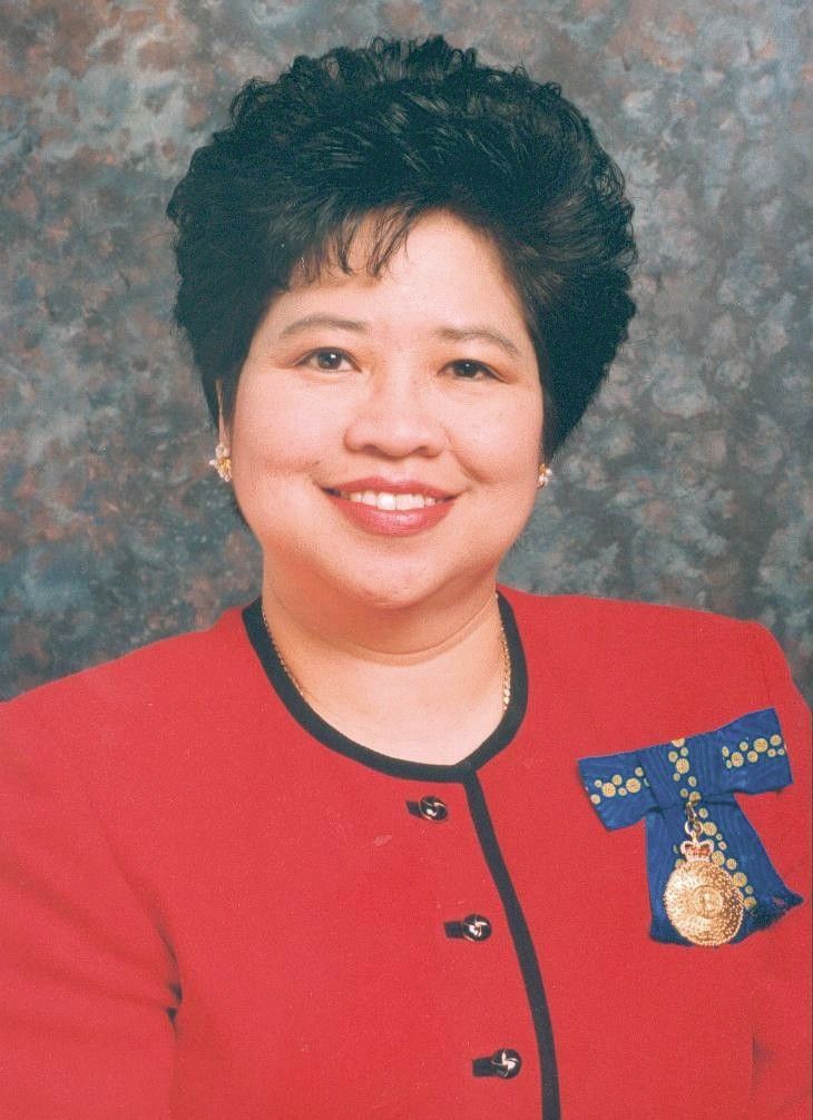 Portrait of a smiling person in a red jacket with a decorative medal pin against a mottled studio backdrop