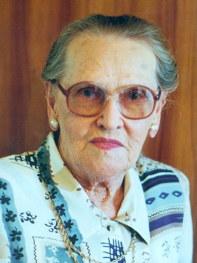 Portrait of an elderly woman wearing glasses and a patterned blouse against a brown background