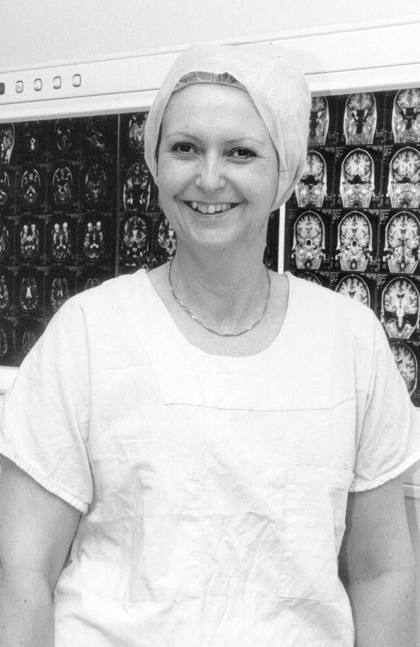 Smiling hospital staff member in scrubs and cap standing in front of medical scans