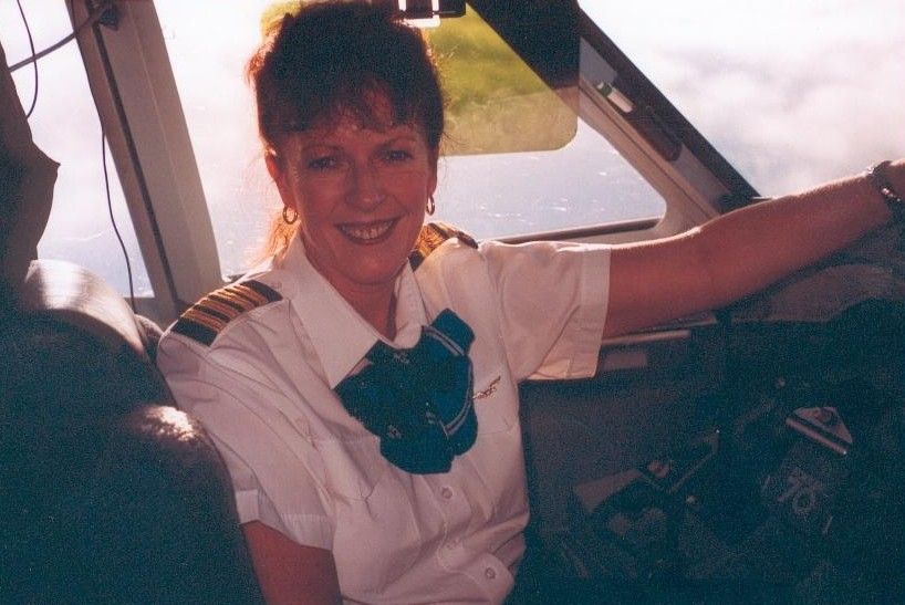 Smiling woman in a white shirt and green scarf sitting in a cockpit or vehicle interior