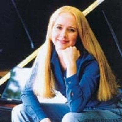 Smiling blonde woman in a blue shirt leaning forward with chin on hand in a modern setting