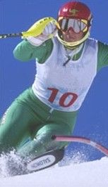 Skier in green suit with red helmet racing downhill through snow, bib number 10 visible
