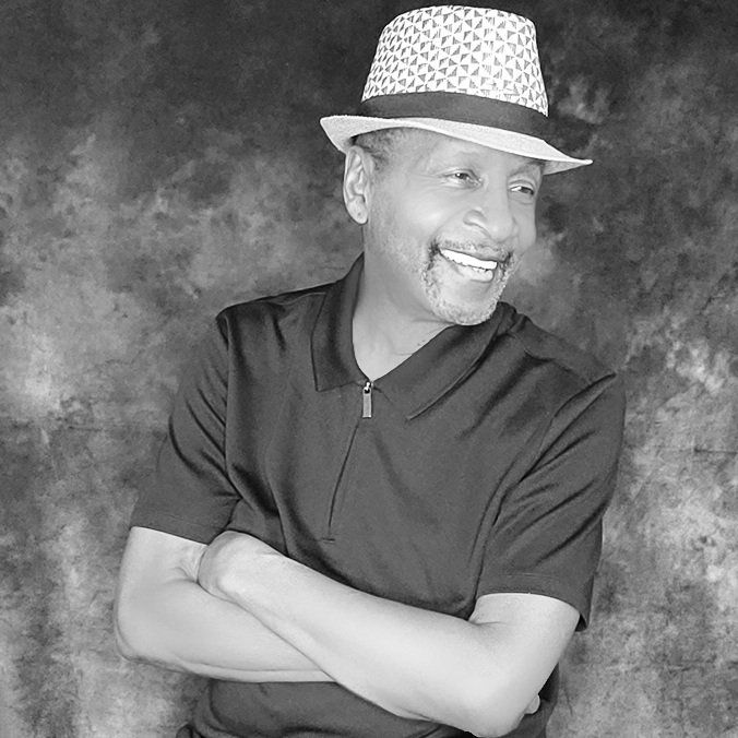 Man in a patterned hat smiling with arms crossed against a textured gray background