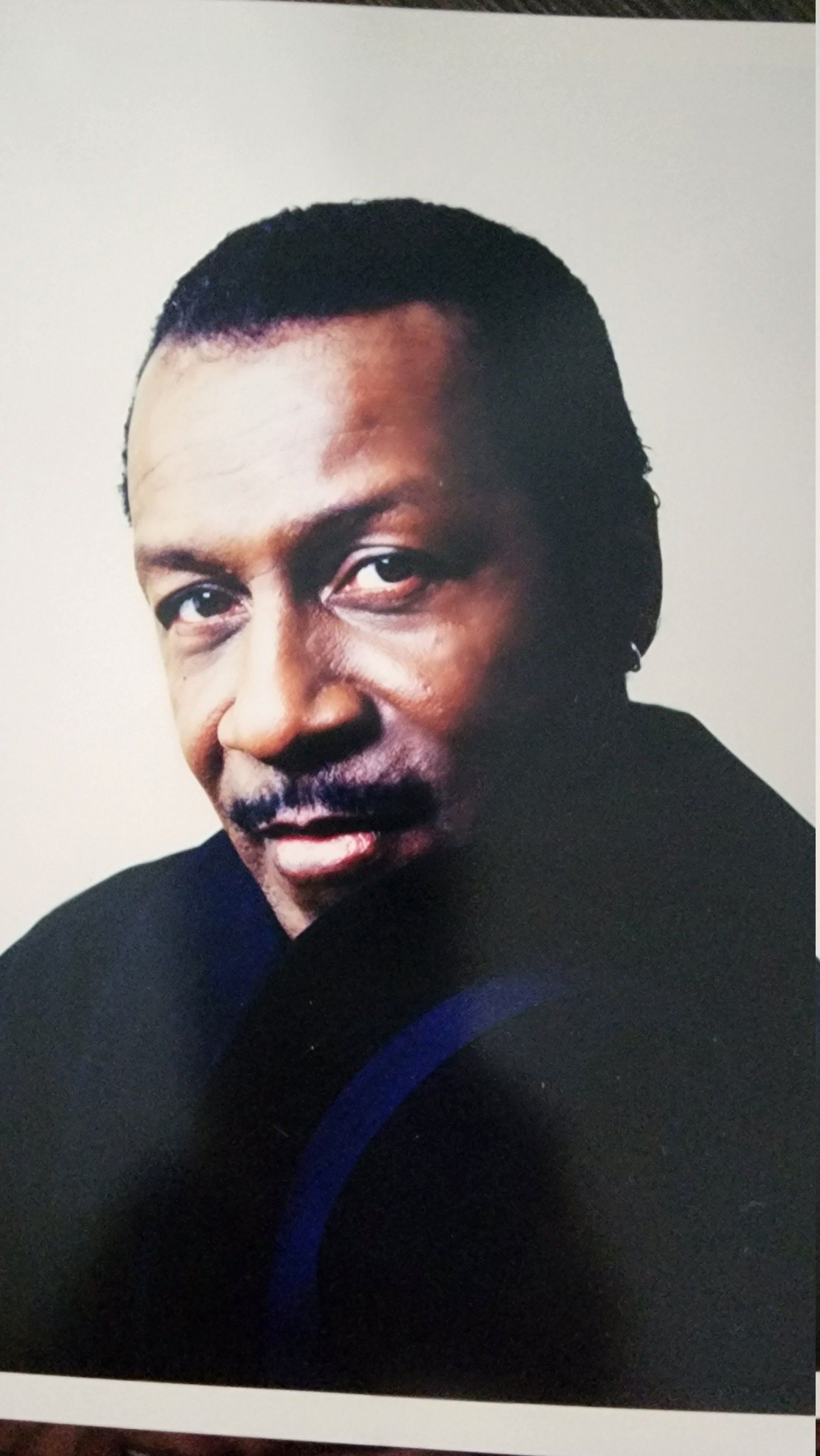 Portrait of a man in a black shirt, looking over his shoulder against a plain white background.