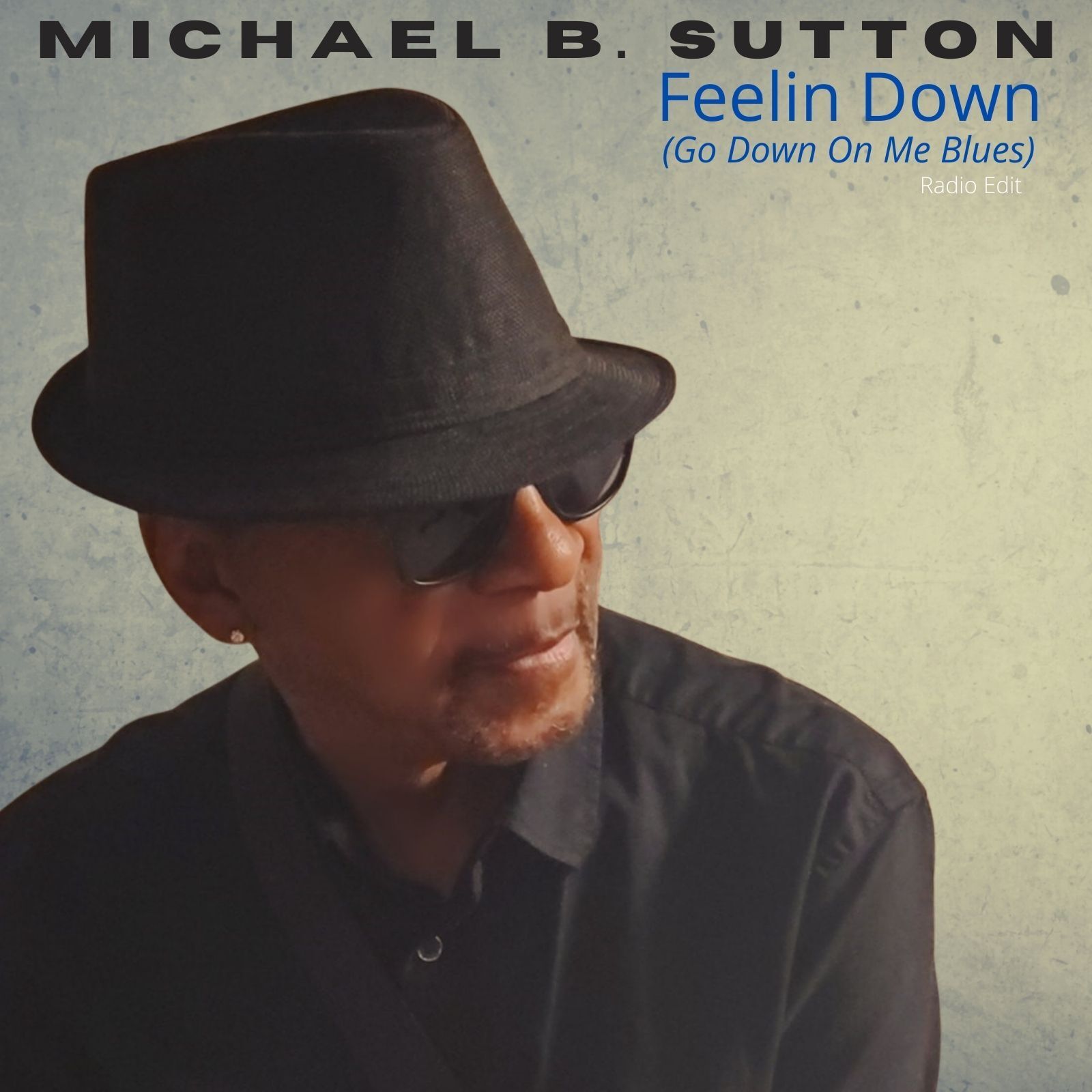 Album cover for Michael B. Sutton’s “Feelin Down (Go Down On Me Blues)” with a man in a black hat and sunglasses.