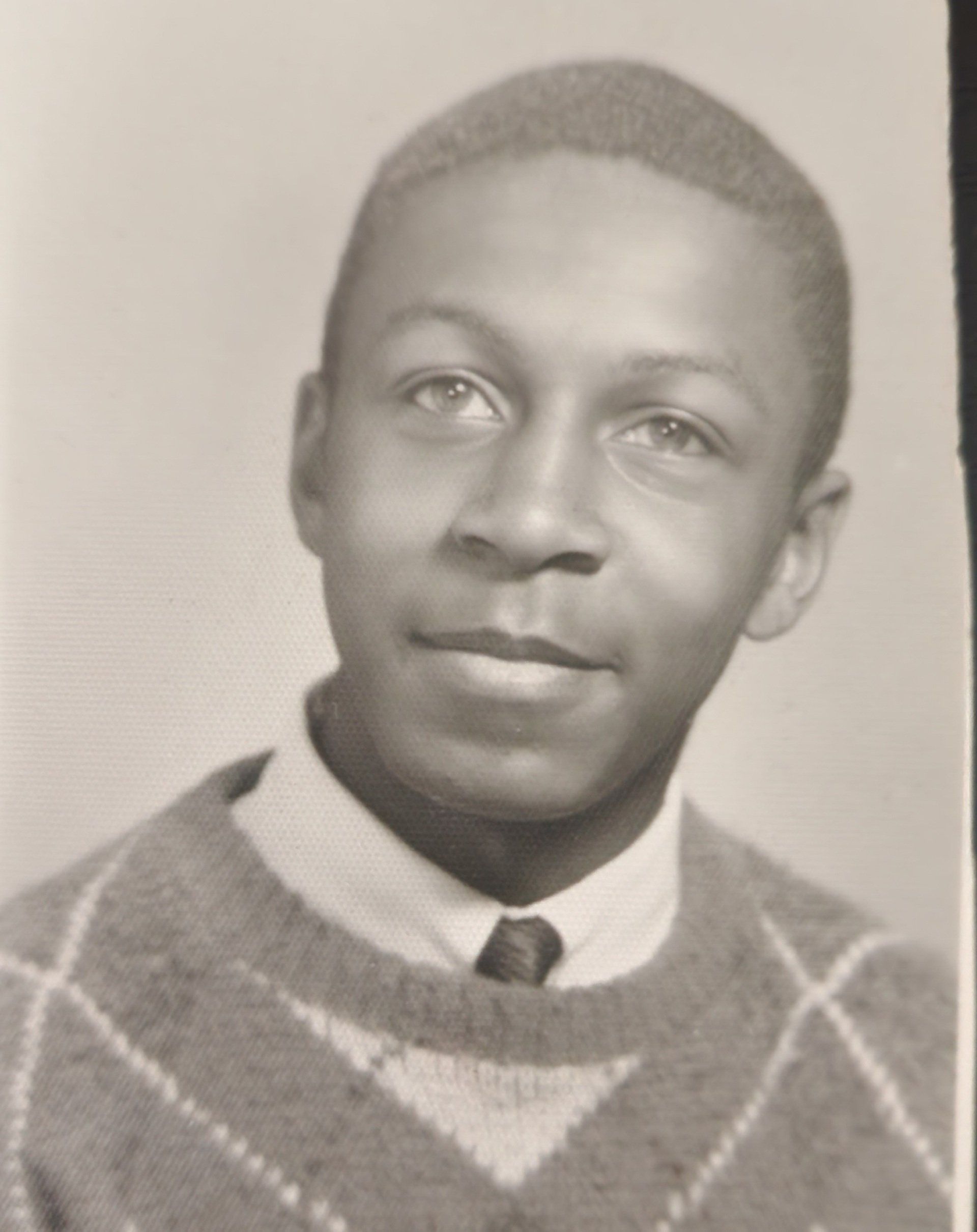 Studio portrait of a person in a patterned sweater, white shirt, and tie, looking slightly upward with a calm expression