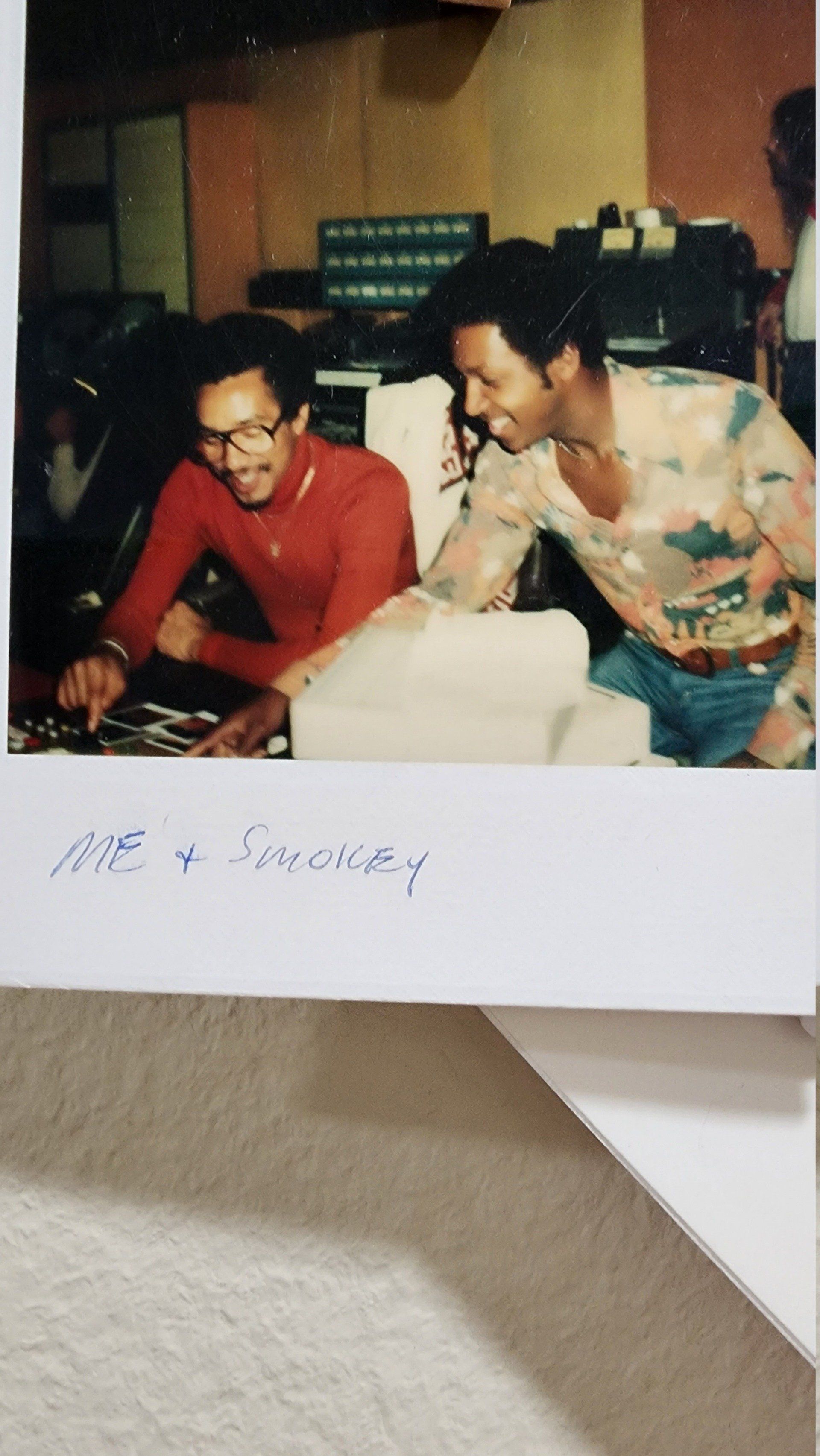 Two people smiling and leaning over a table in a casual indoor setting, with handwritten text at the bottom.
