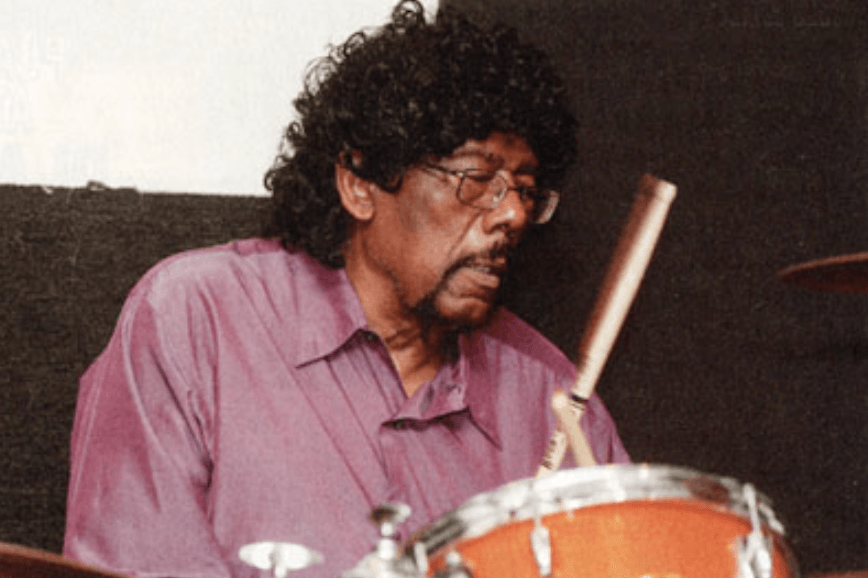 Drummer in a pink shirt playing an orange drum set, focused on the performance