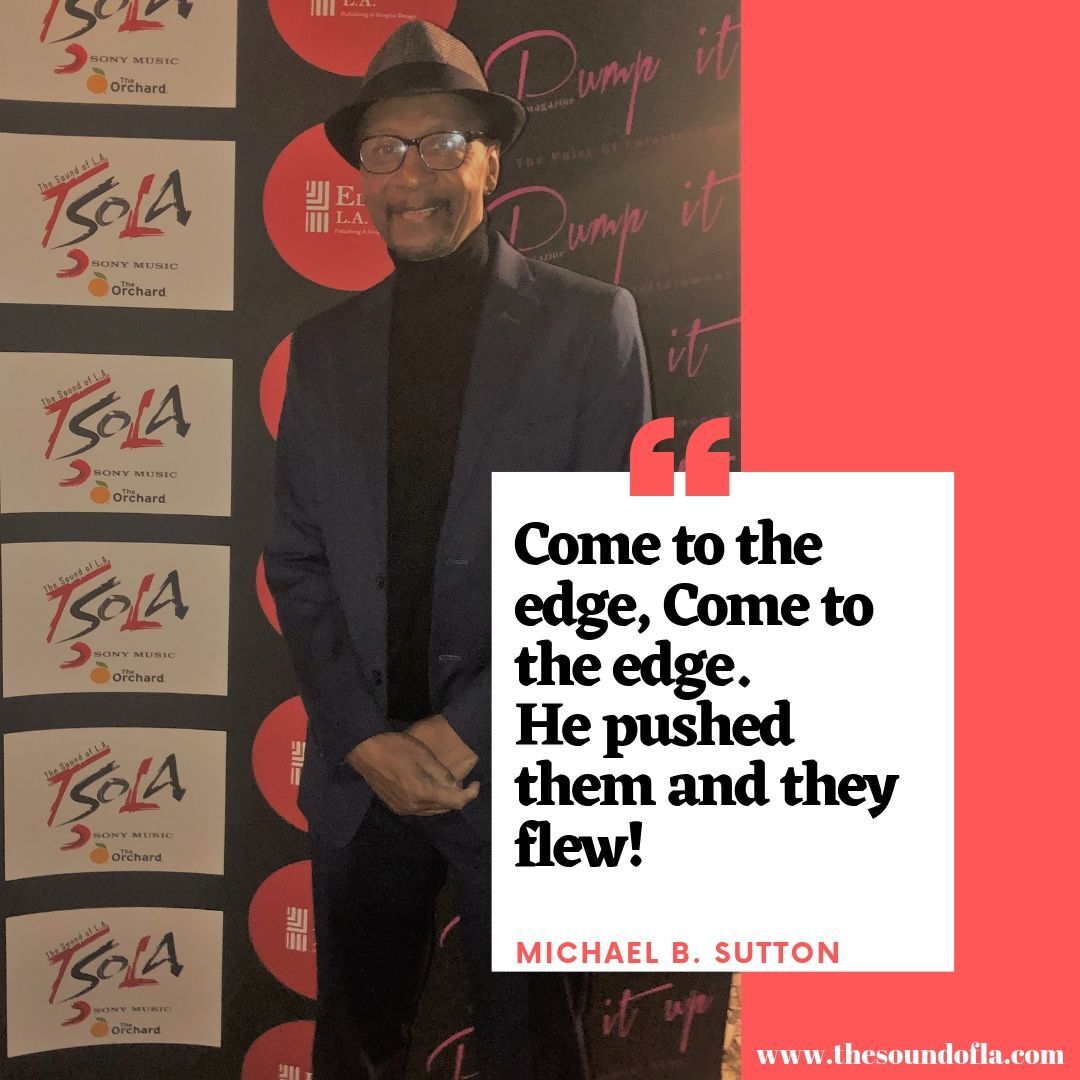 Man in dark suit and cap at event backdrop, beside quote: “Come to the edge. Come to the edge. He pushed them and they flew!”