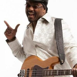 Smiling musician in a hat playing a tan electric guitar and pointing upward