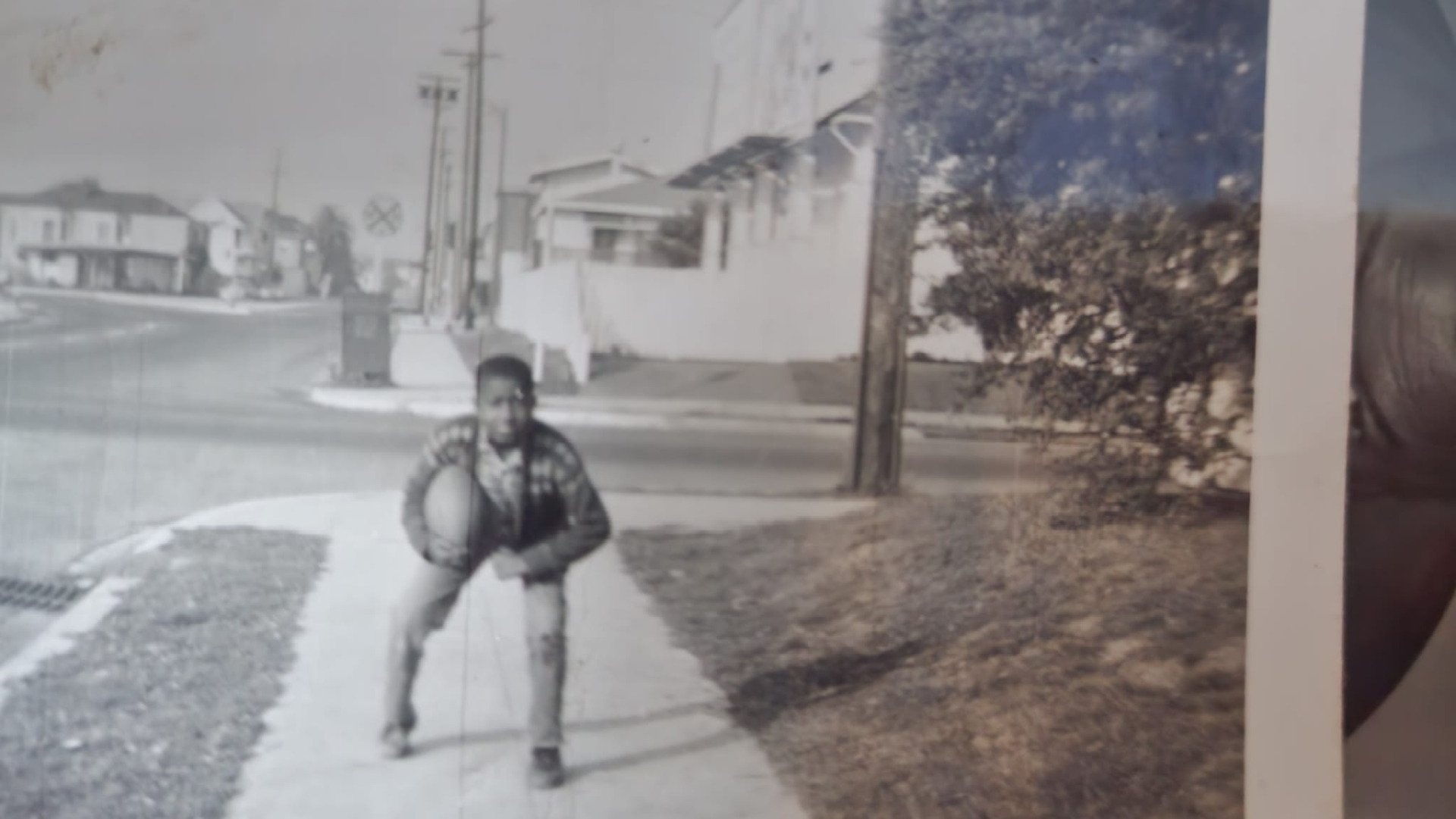 Child crouching on a suburban sidewalk beside a parked car, with houses and trees in the background