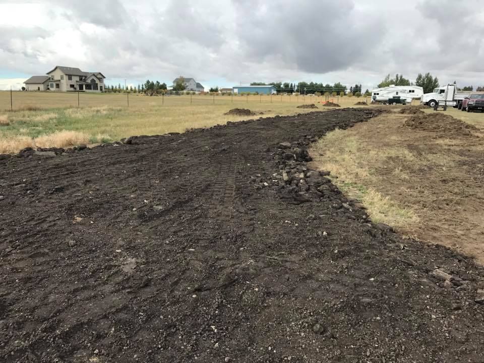 A wide, unpaved dirt path under a cloudy sky, with fields and houses in the distance.