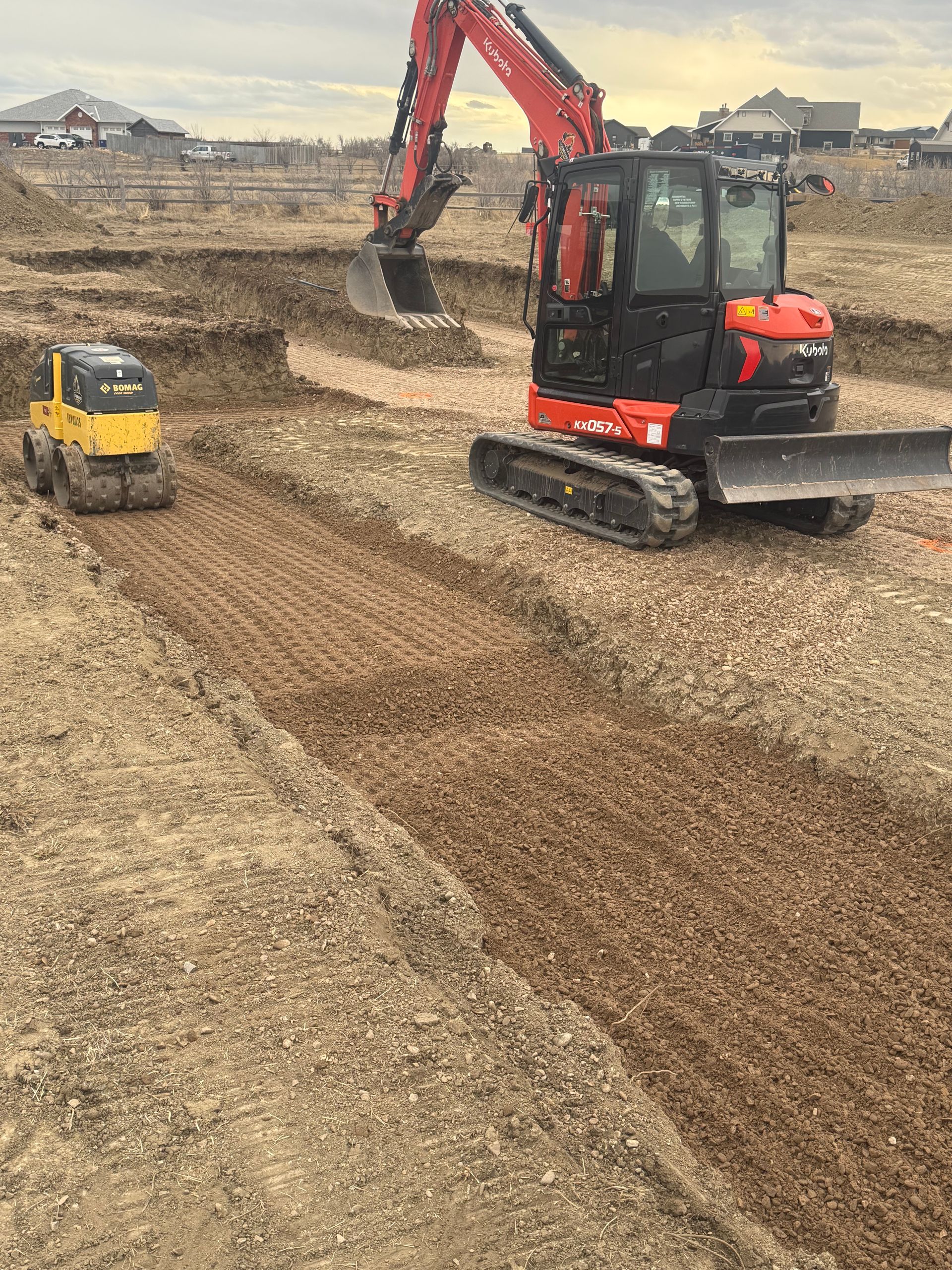 A red excavator and a smaller yellow piece of construction equipment work on a gravel construction site.