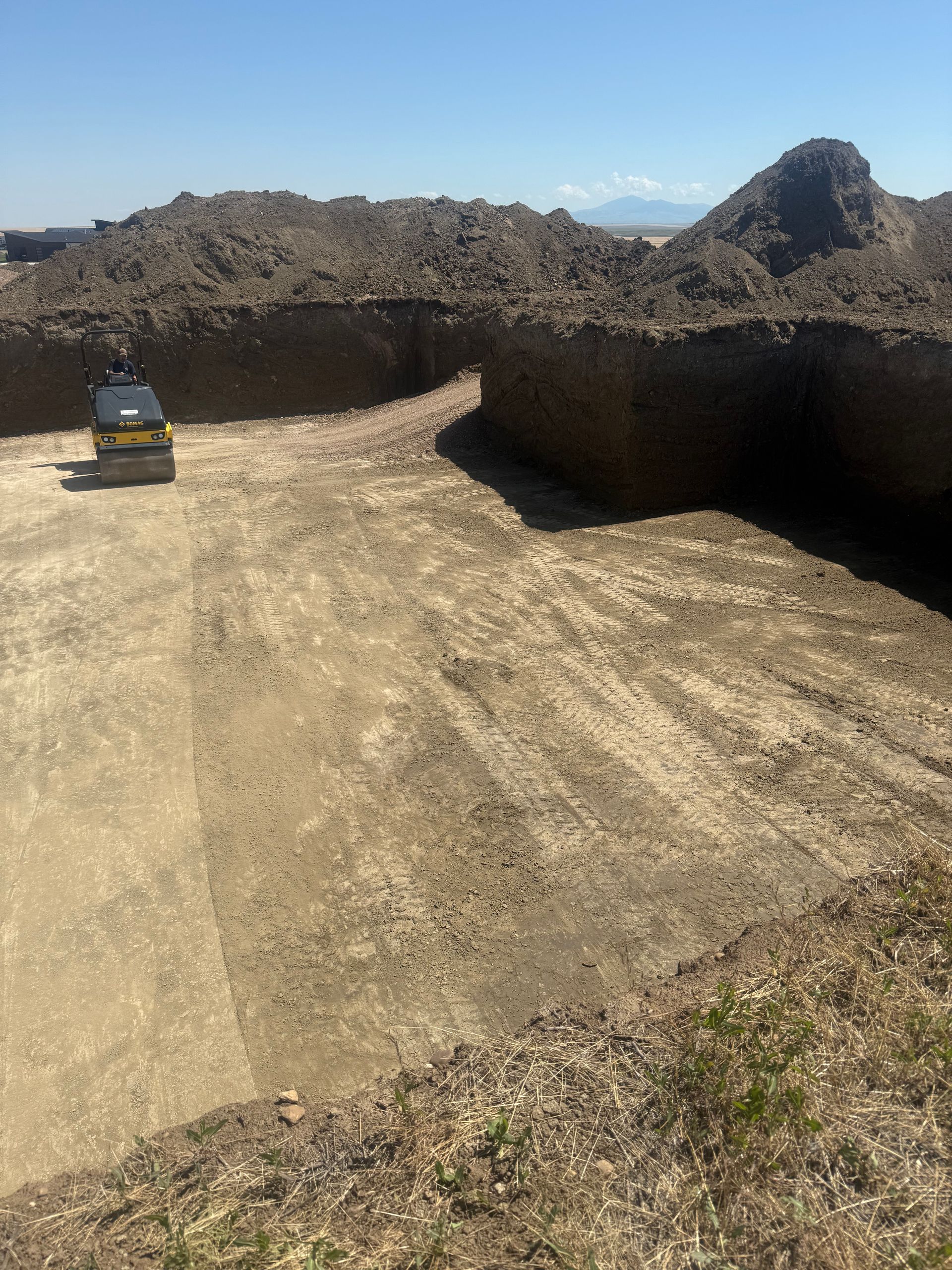 A small yellow construction roller sits in a large, excavated dirt pit under a clear blue sky.