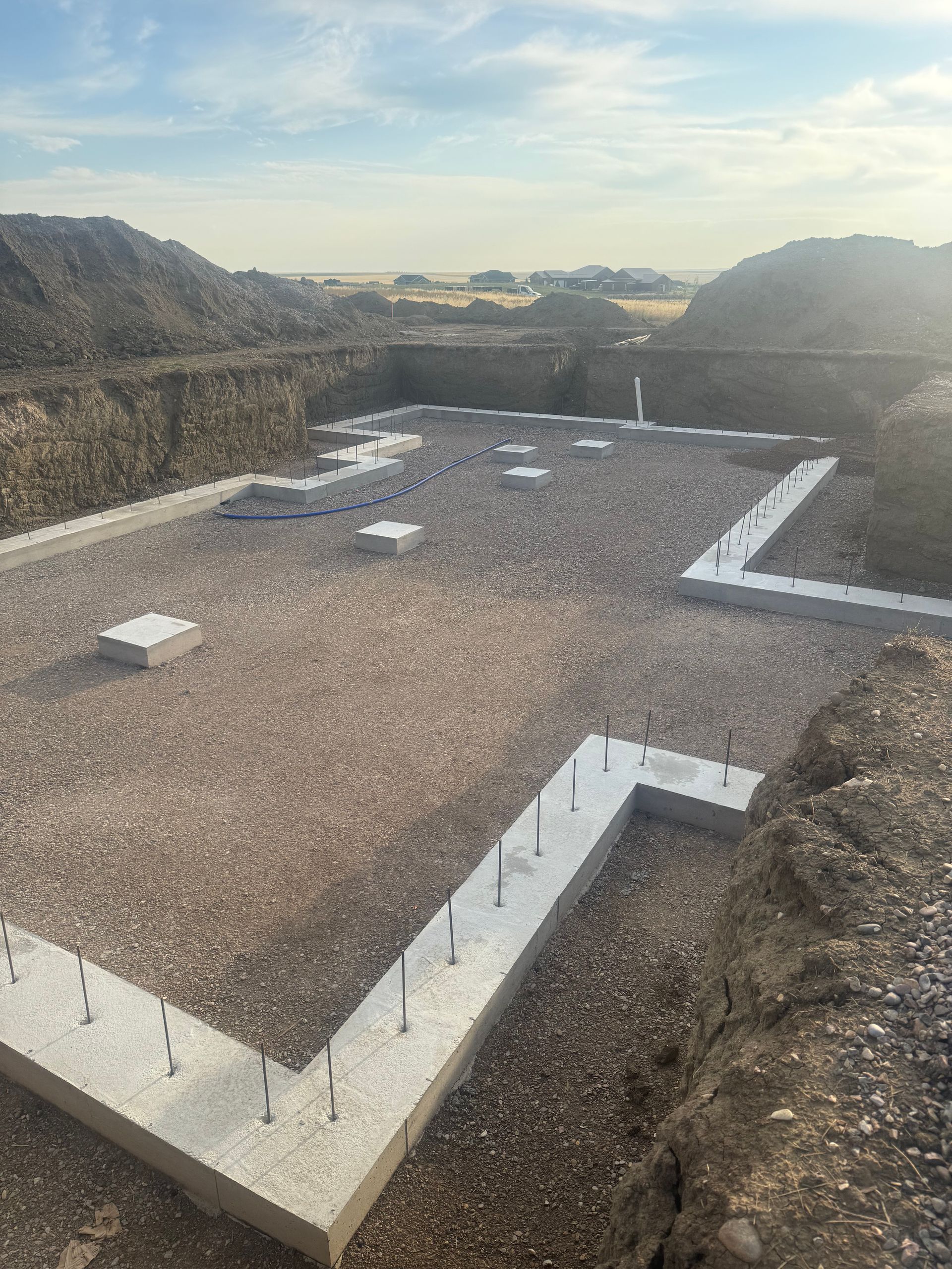 A construction site showing concrete foundations and footings set into a gravel-filled excavated area.