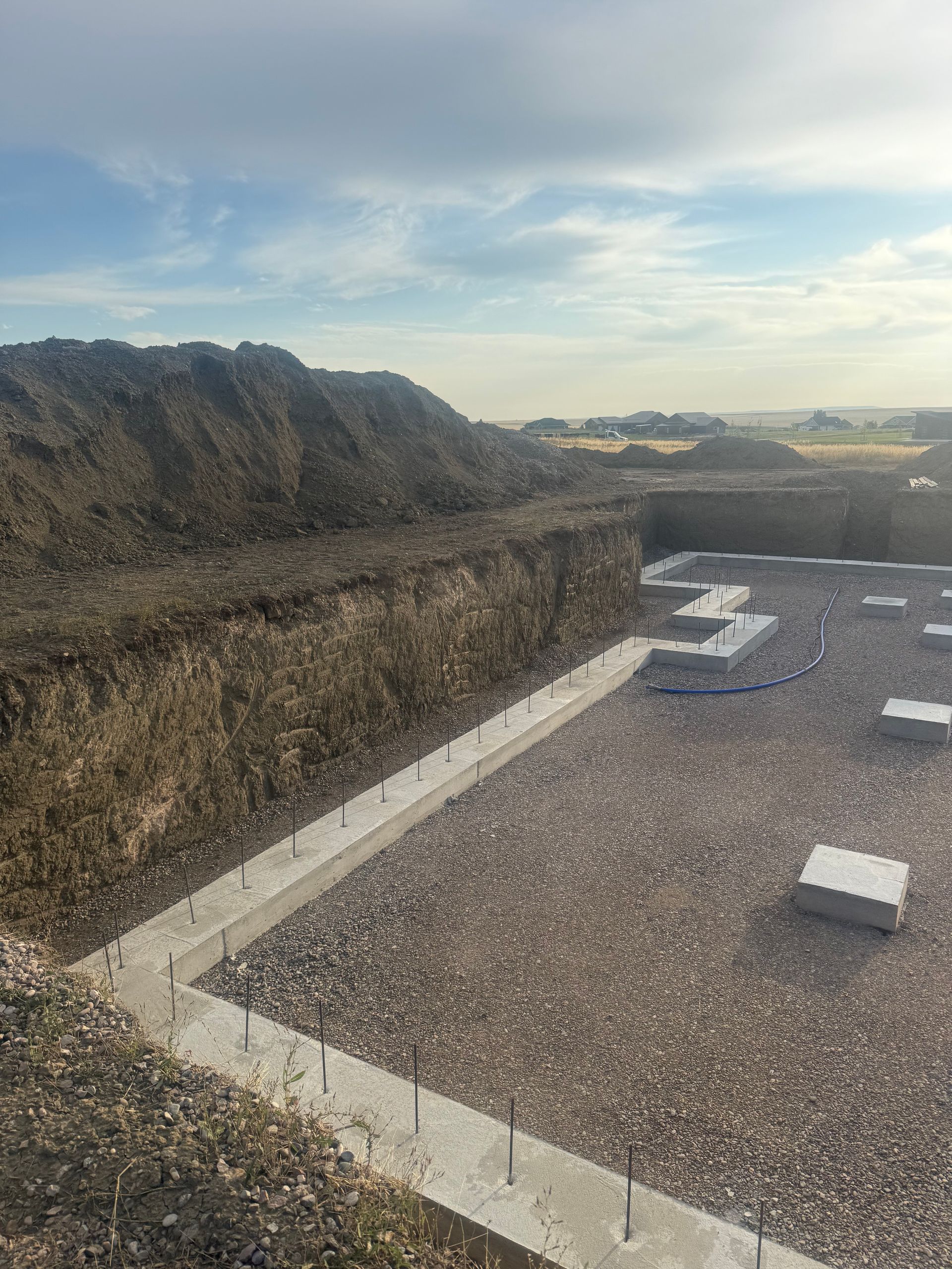 A construction site showing concrete foundations and footings set within a large excavated earth pit.