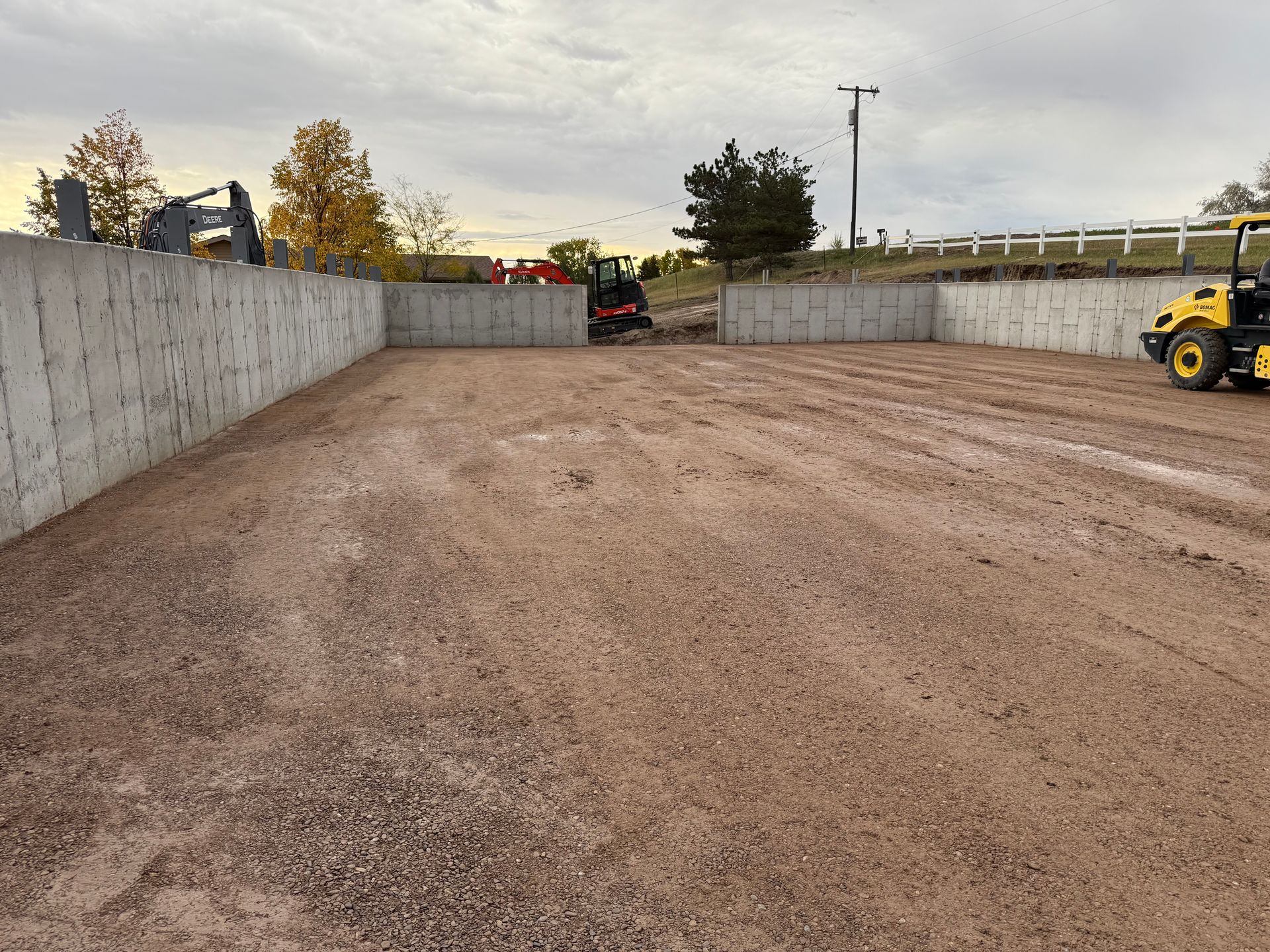 Construction site with a gravel ground, concrete foundation walls, and heavy machinery on an overcast day.