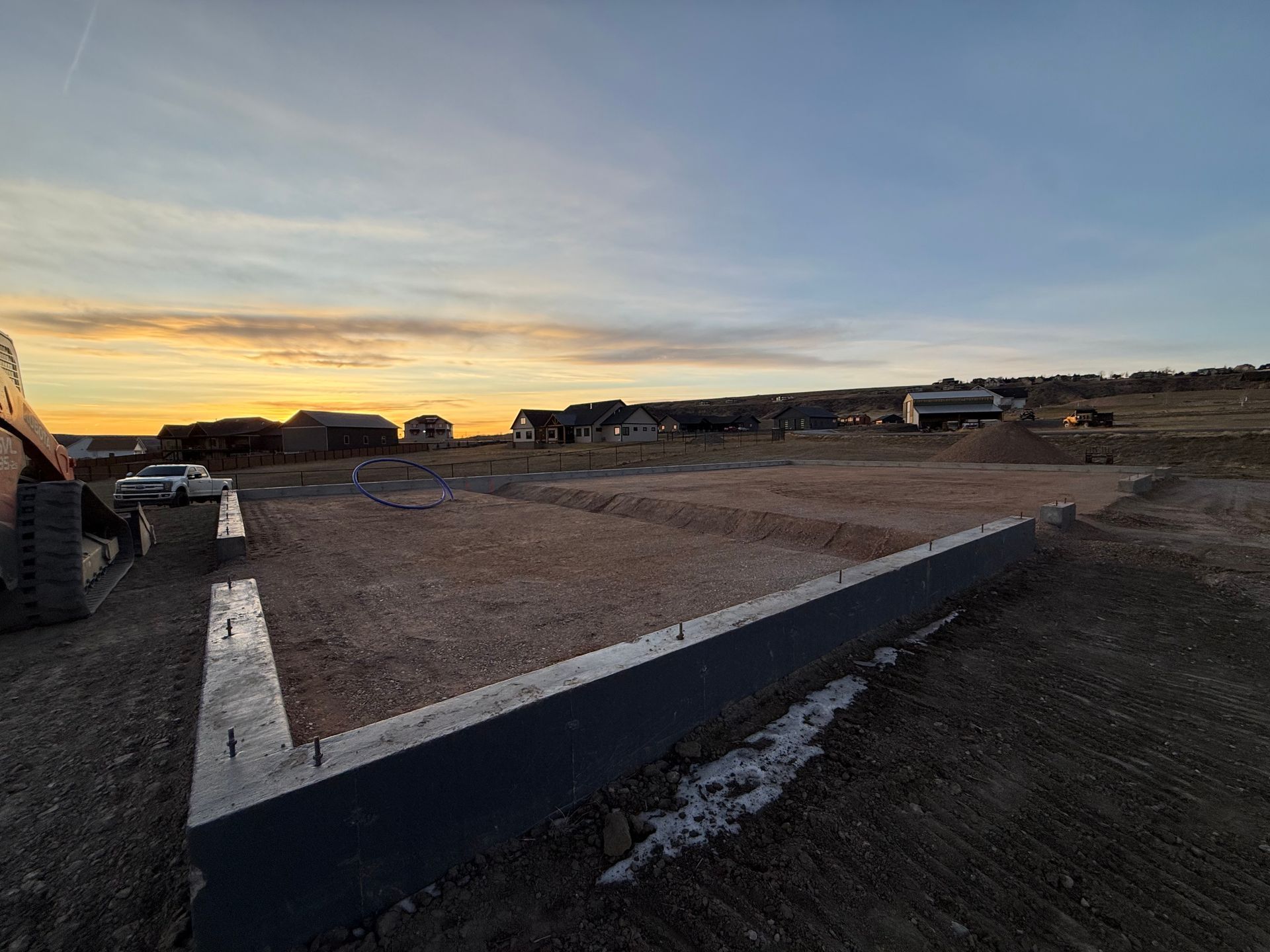 A concrete foundation for a new house at a construction site under a sunset sky.