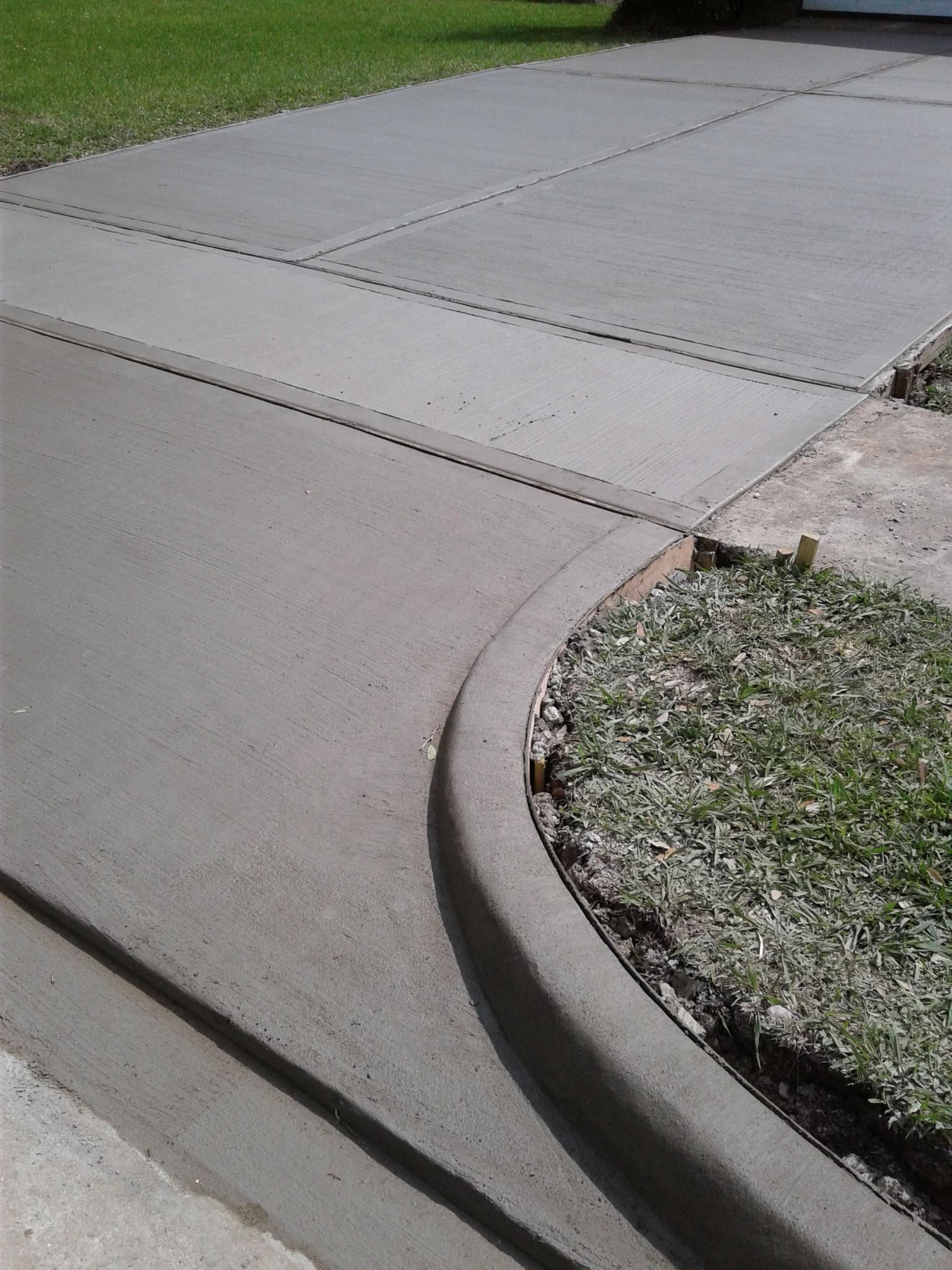 Newly poured concrete driveway with a rounded curb next to a patch of grass.