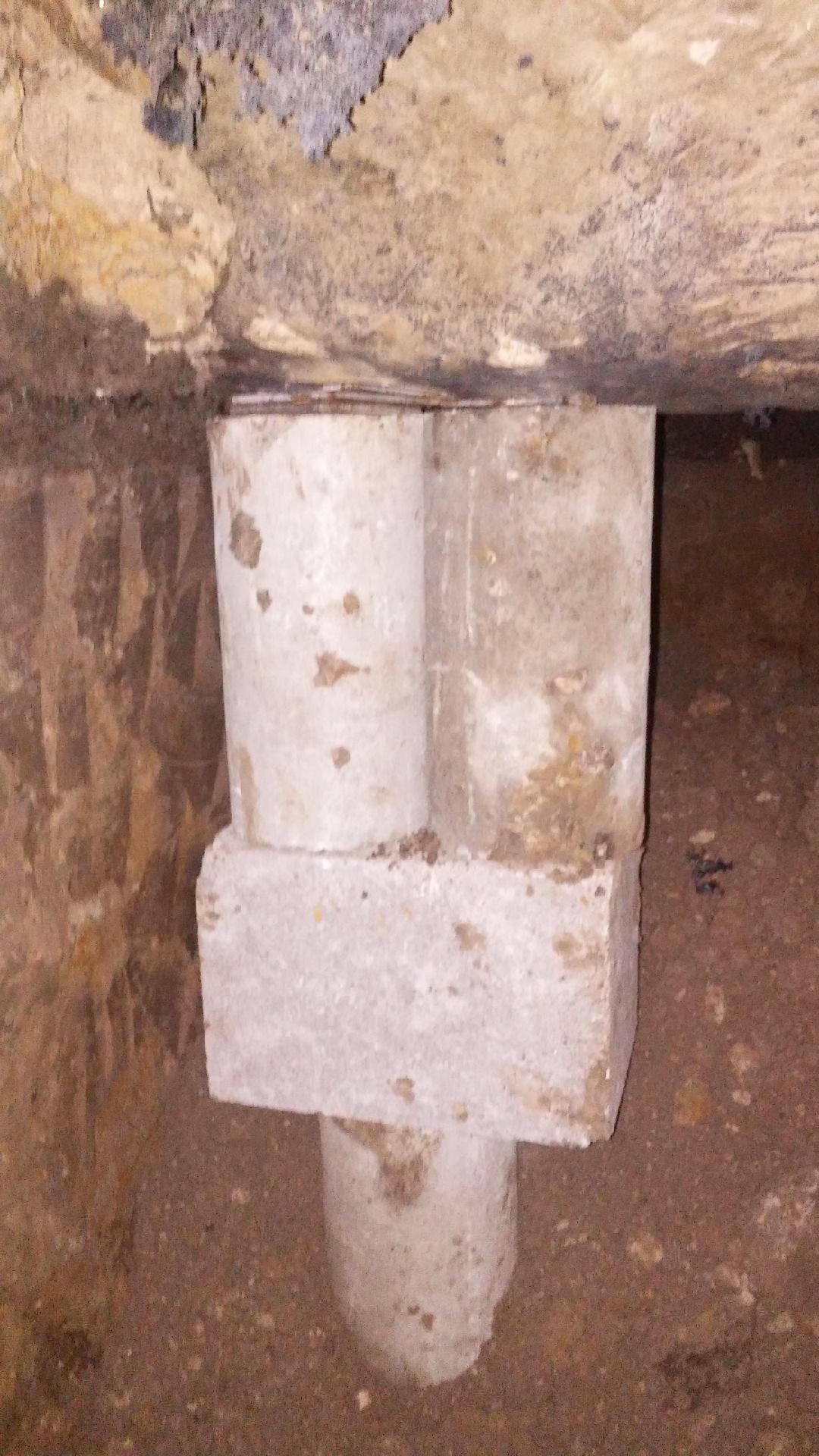 Vertical view of white PVC plumbing pipes connected to a block and below ground, possibly a drain.