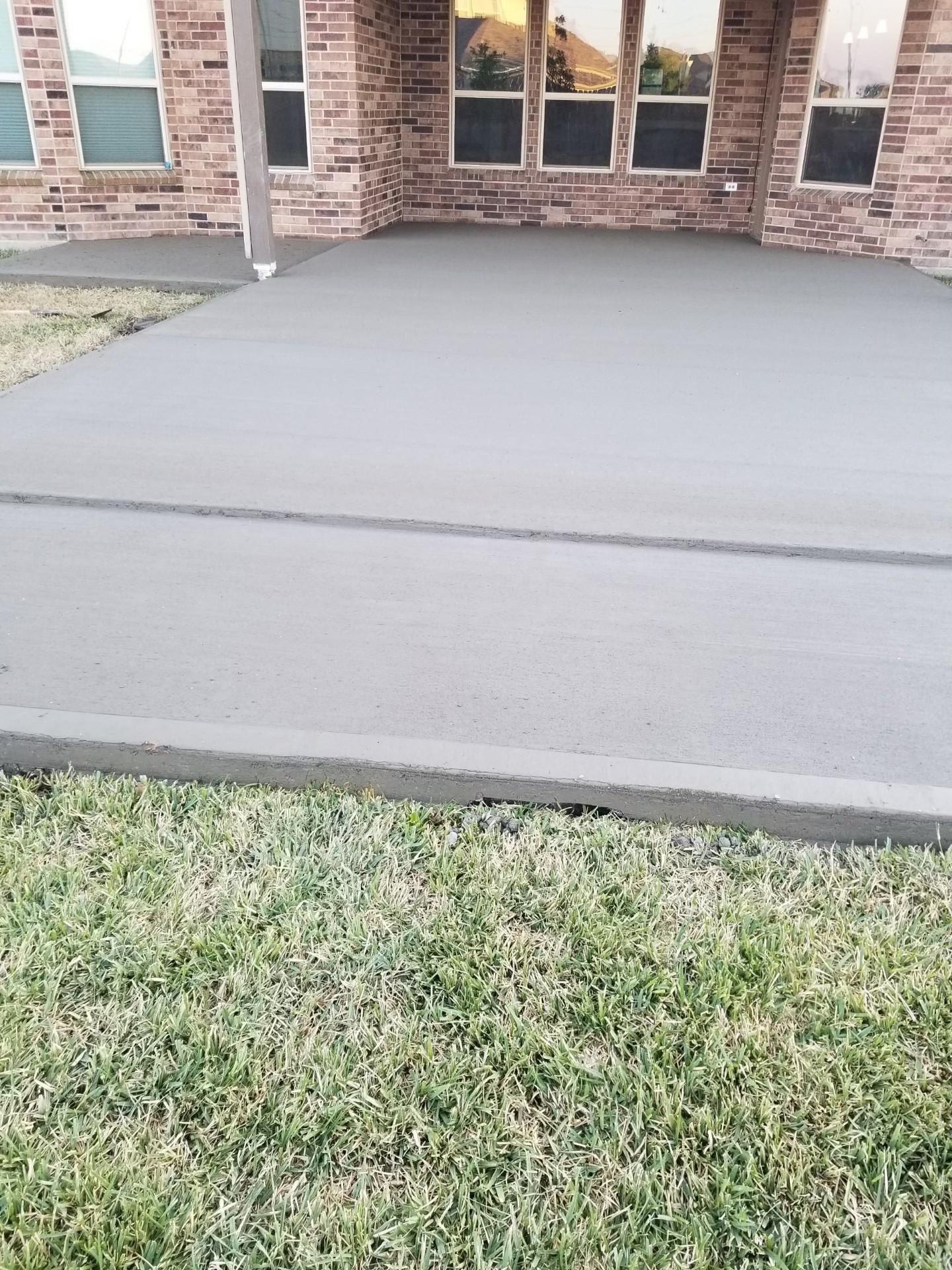 Newly poured concrete patio next to a lawn and a brick house.