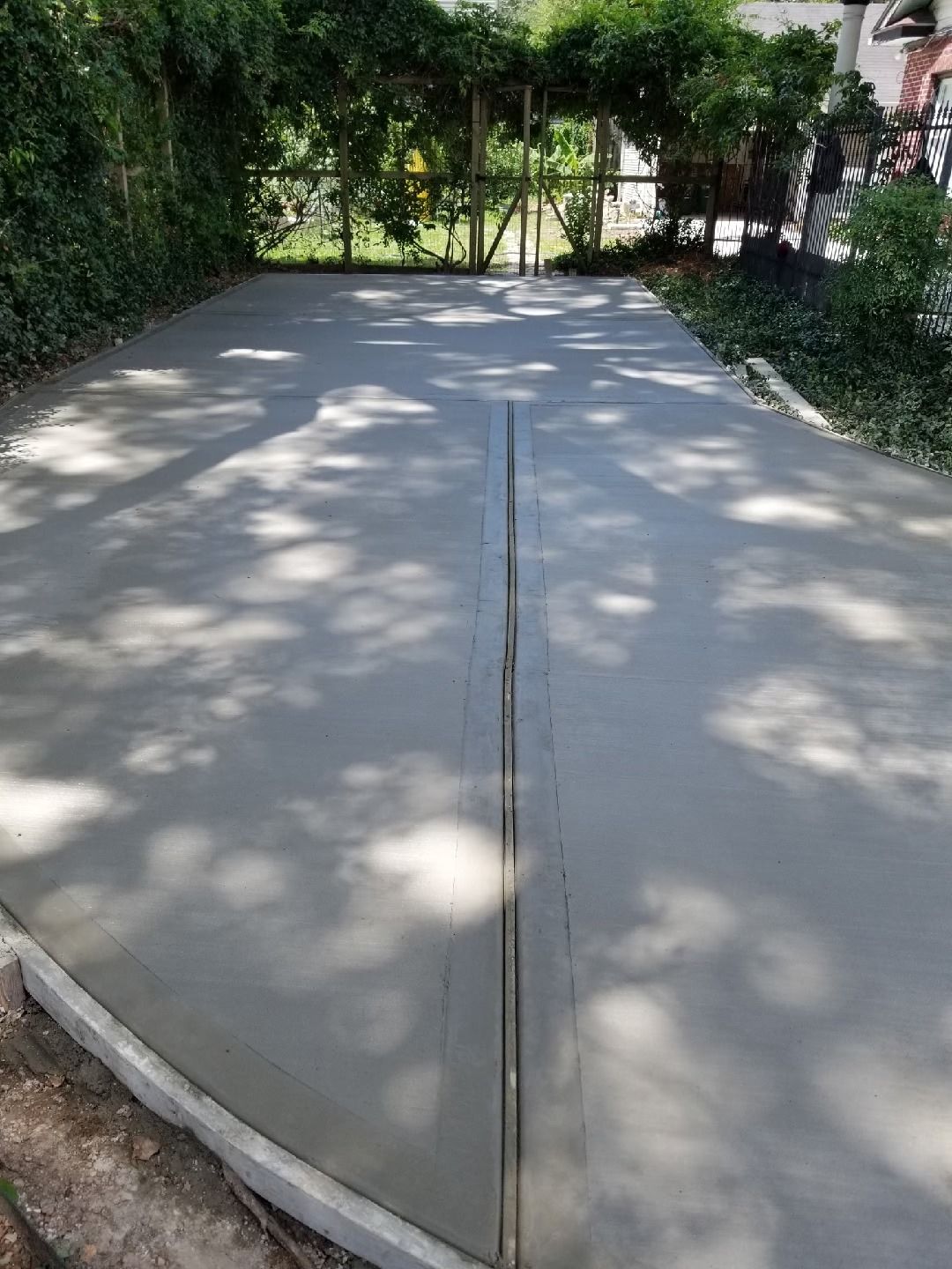 Newly poured concrete driveway with a central seam, edged by a low curb, under a shaded canopy.
