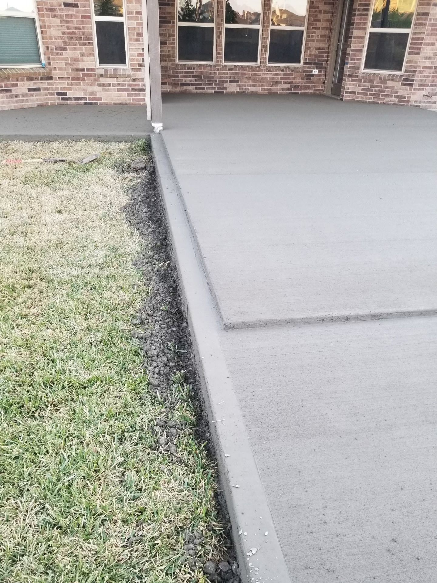 Concrete patio next to grass, with a brick building in the background.