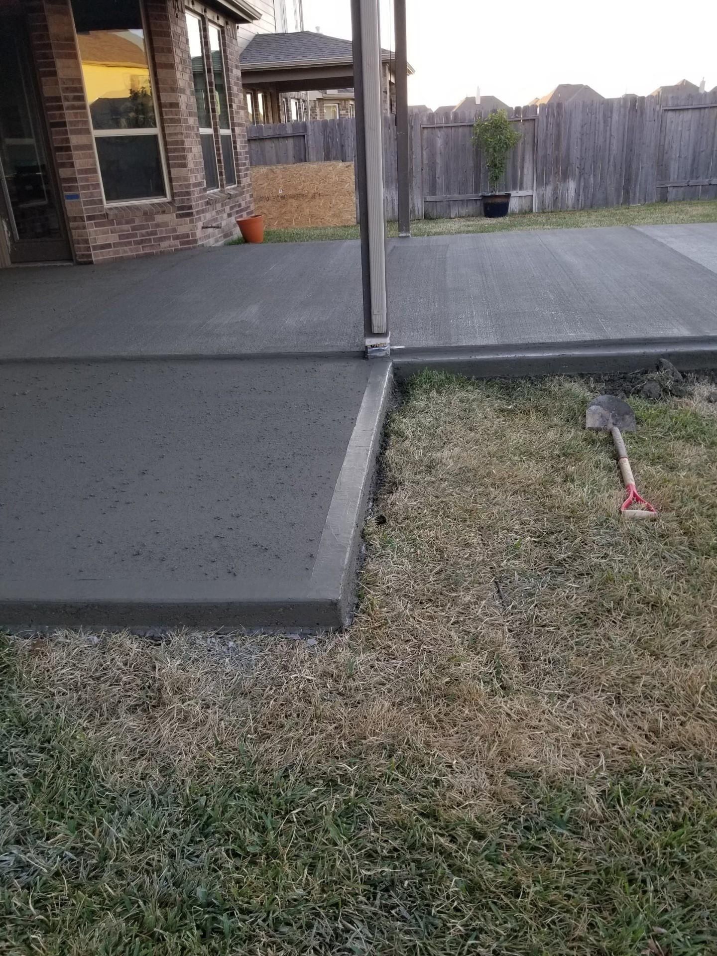 Newly poured concrete patio next to dry grass in a backyard.