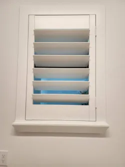 White plantation shutters over a window with a small shelf beneath it, showing blue sky outside
