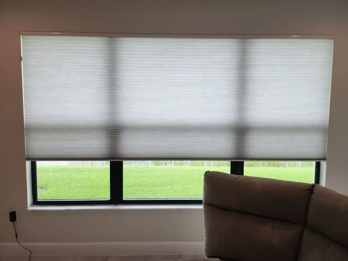 Living room window with white blinds partially open above a dark sectional sofa