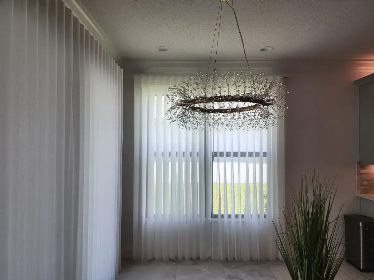 Modern dining room with sheer curtains, a pendant chandelier, and a potted plant by the window
