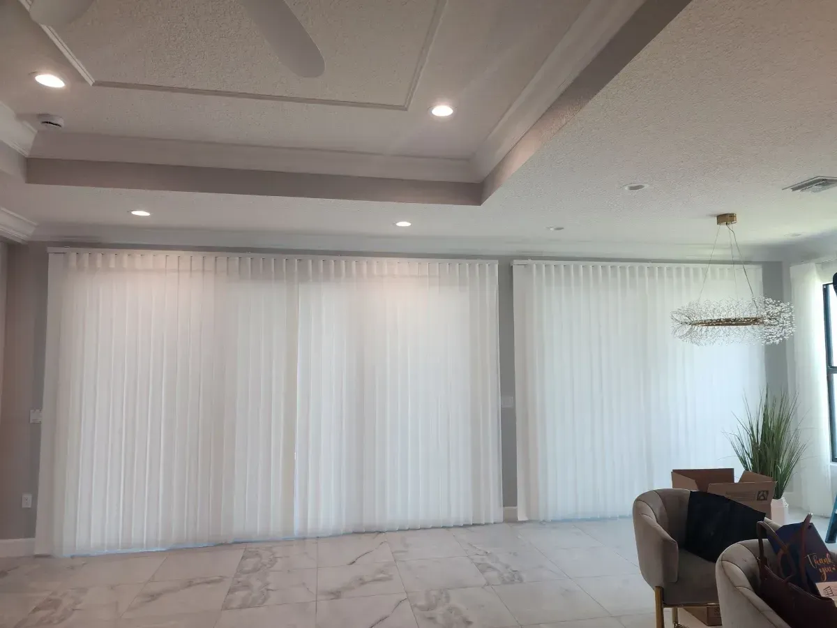 Spacious modern living room with white curtains, marble floor, recessed ceiling lights, and a sofa by the window