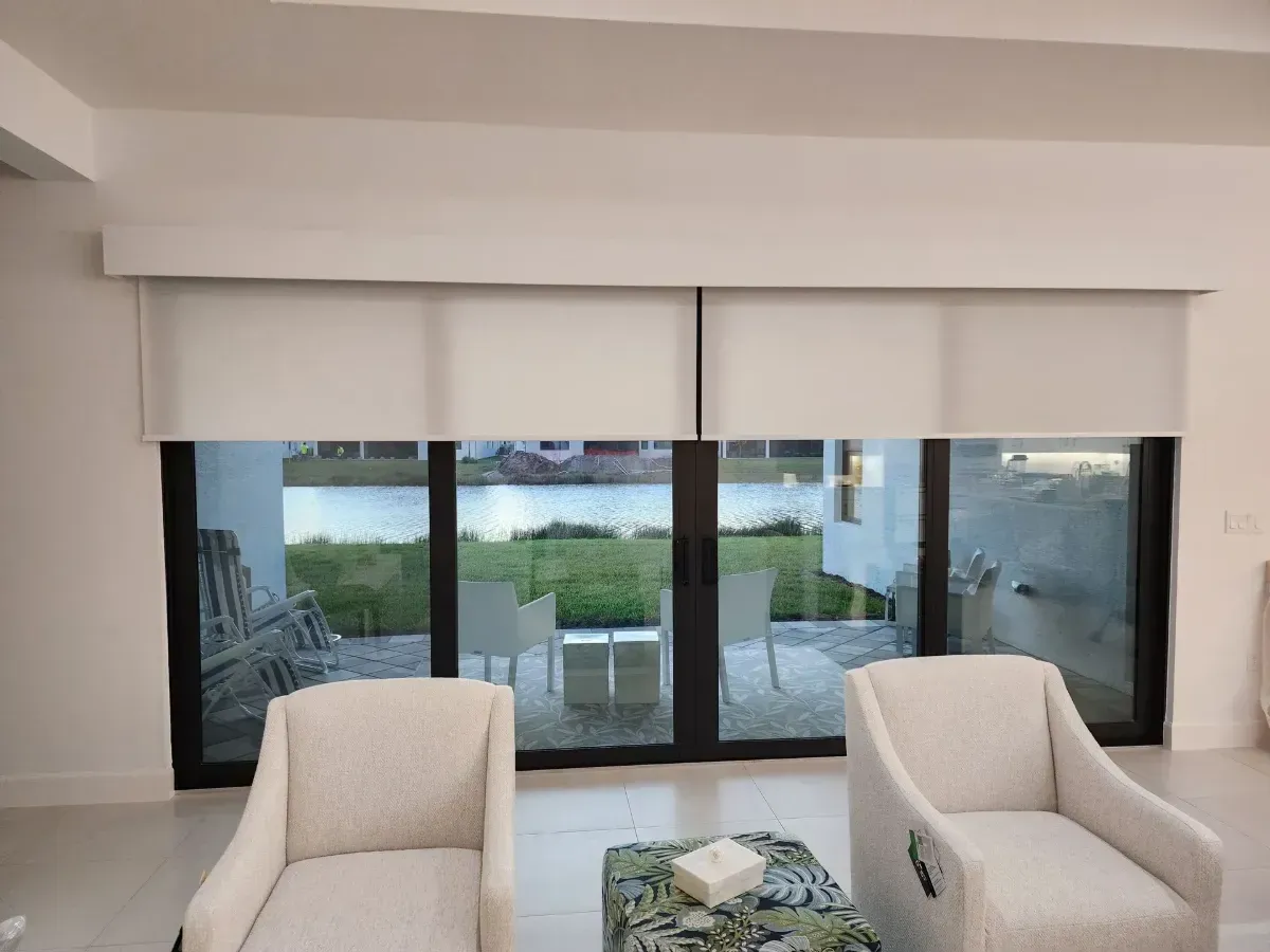 Modern living room with two cream armchairs, a glass coffee table, and sliding doors to a patio with water view