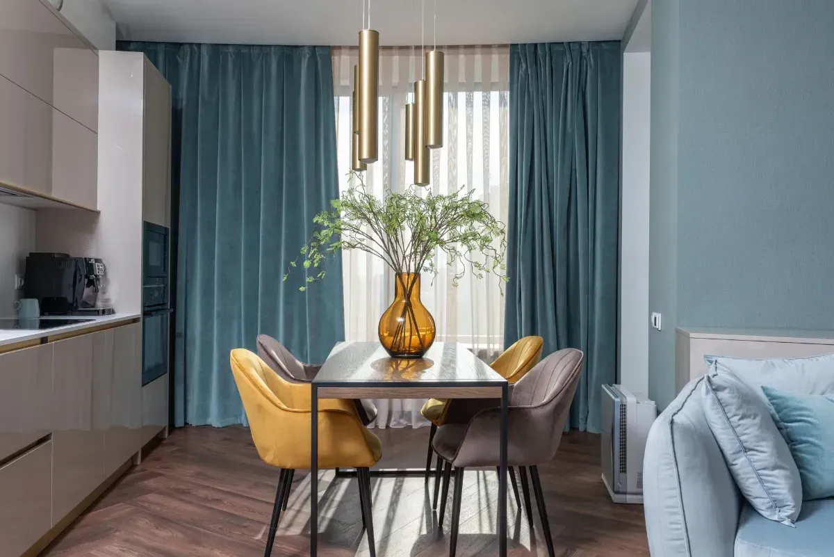 Modern dining room with blue curtains, yellow chairs, and a vase on the table