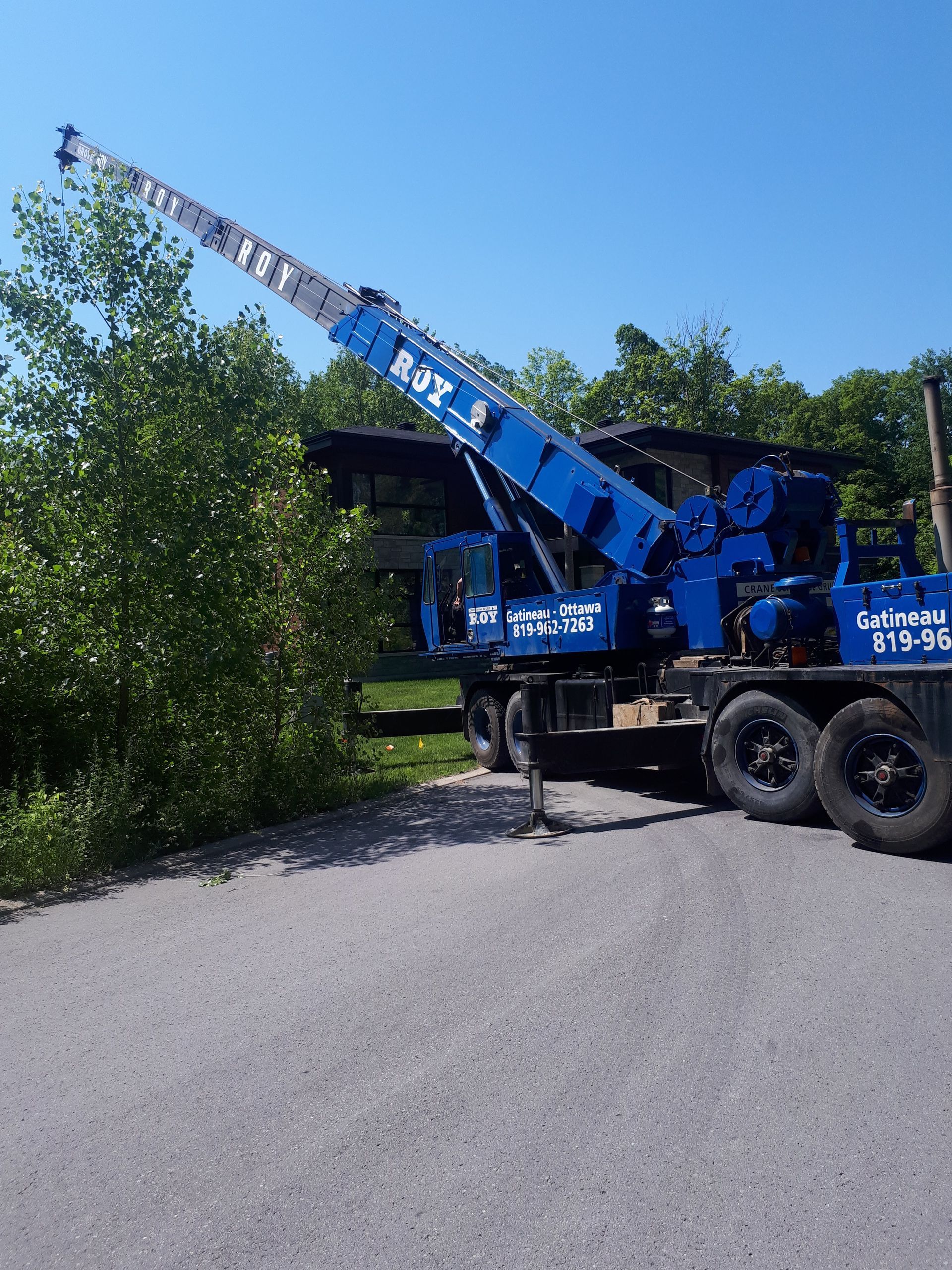 Une grue mobile bleue se dresse sur une surface de gravier sous un ciel bleu clair, sa flèche télescopique déployée vers le haut.
