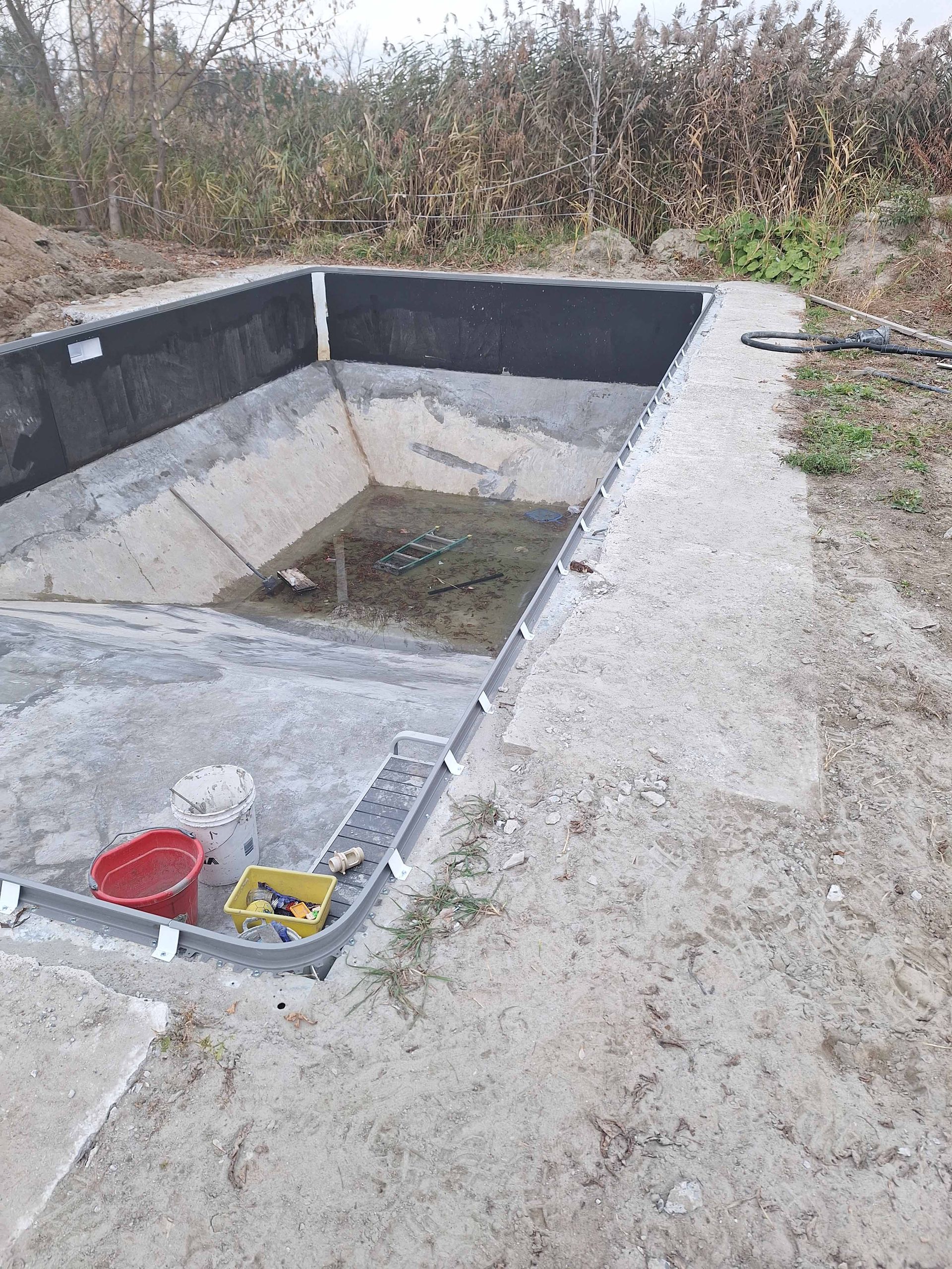 Une piscine rectangulaire en béton, inachevée et en construction sur un terrain vague.