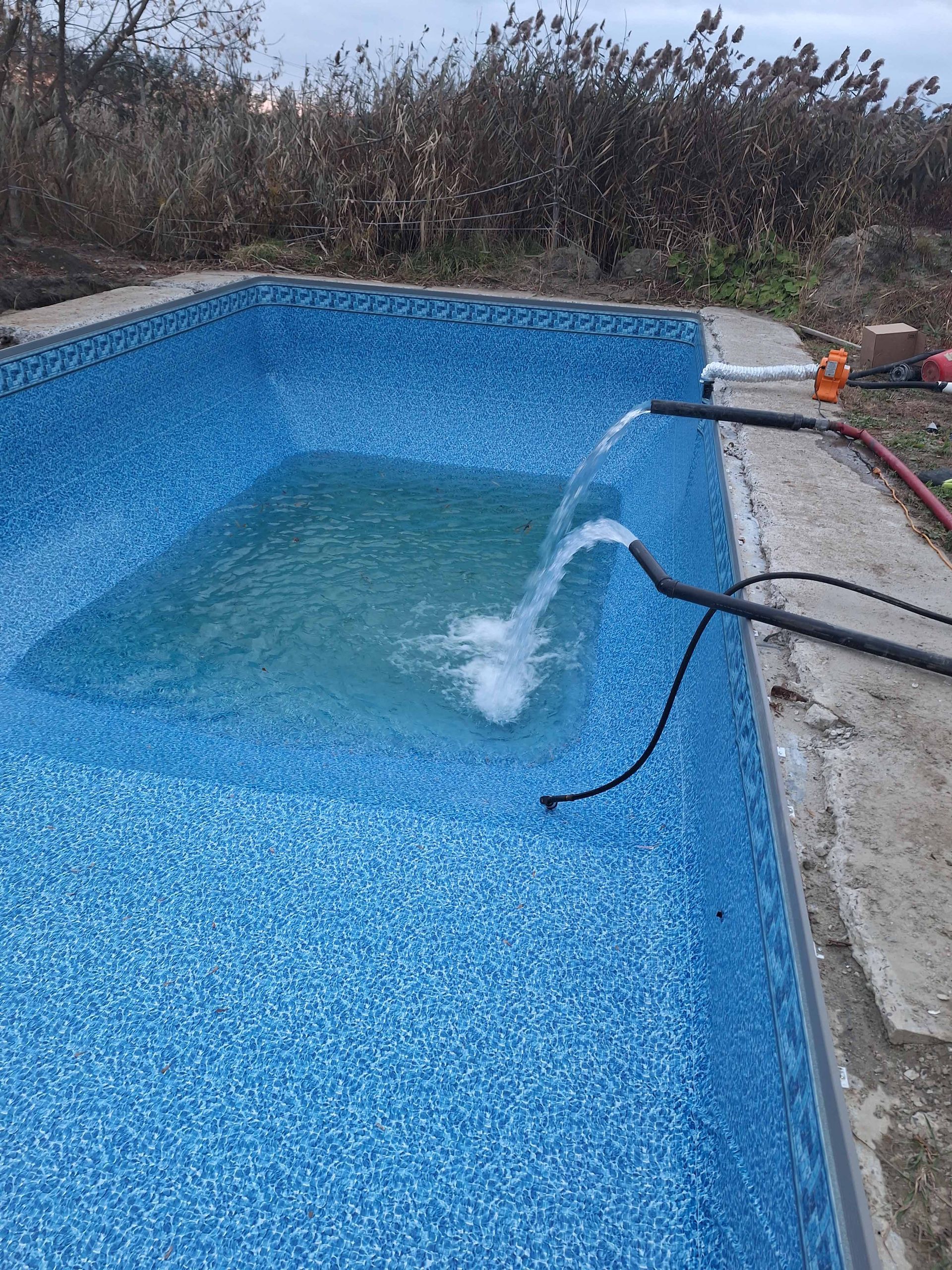 Deux tuyaux déversent de l'eau dans une piscine extérieure rectangulaire carrelée de bleu.