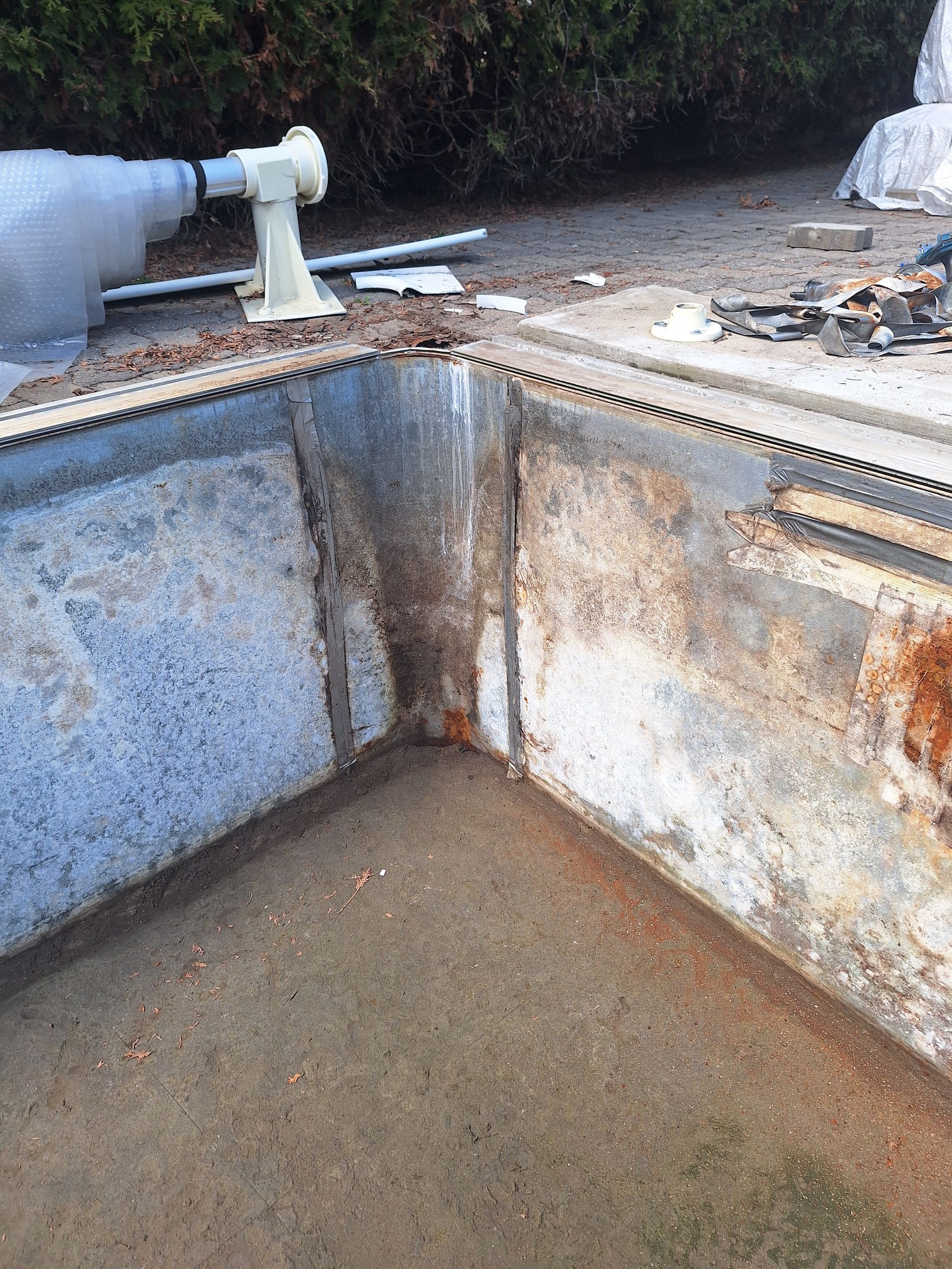 Un coin d'une piscine en béton vide et délabrée, en cours de réparation, avec des fissures visibles et des surfaces usées.