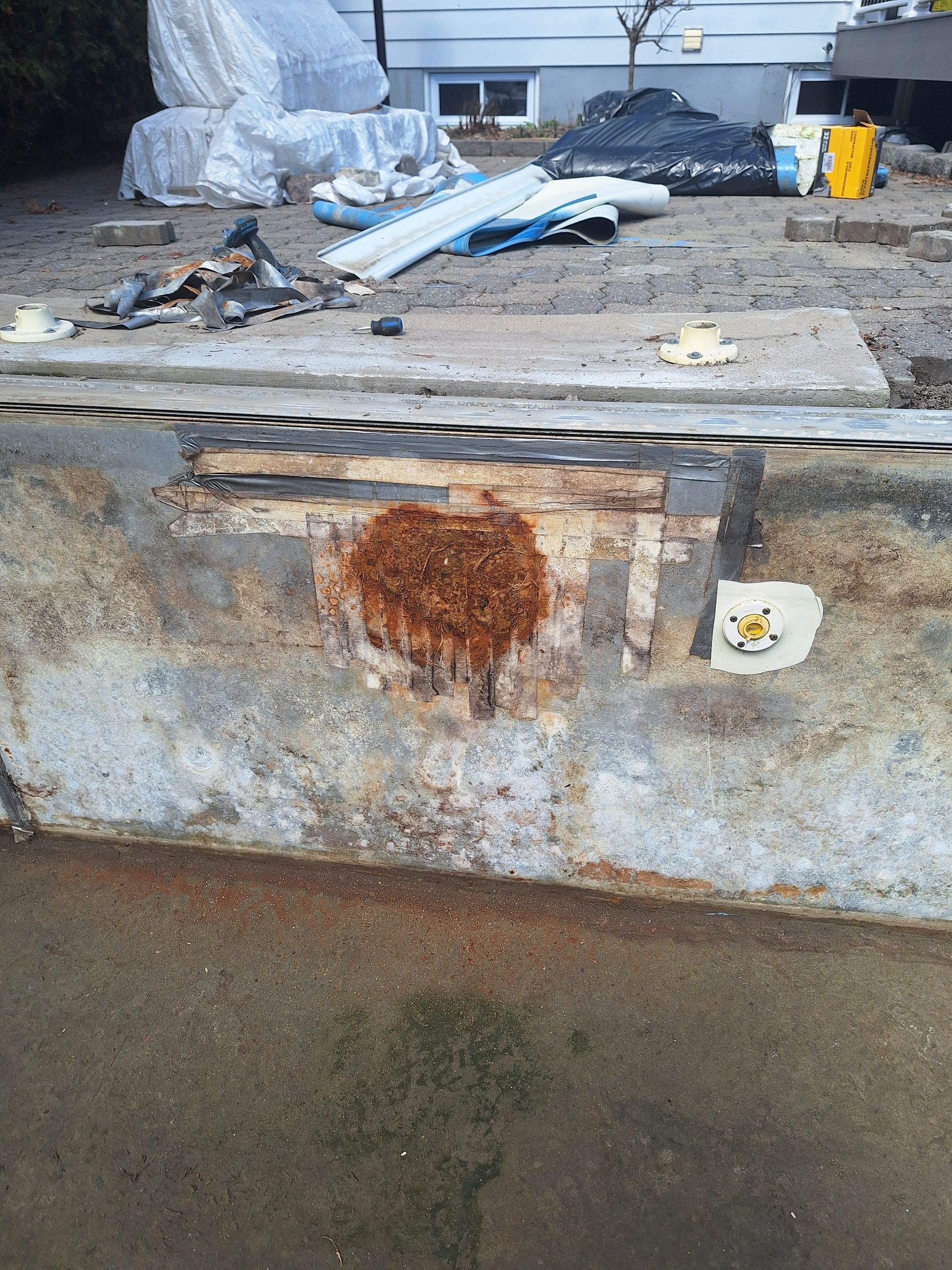 Un muret de soutènement en béton bas, taché d'une tache brun orangé ressemblant à de la rouille, et un élément circulaire mal fixé.