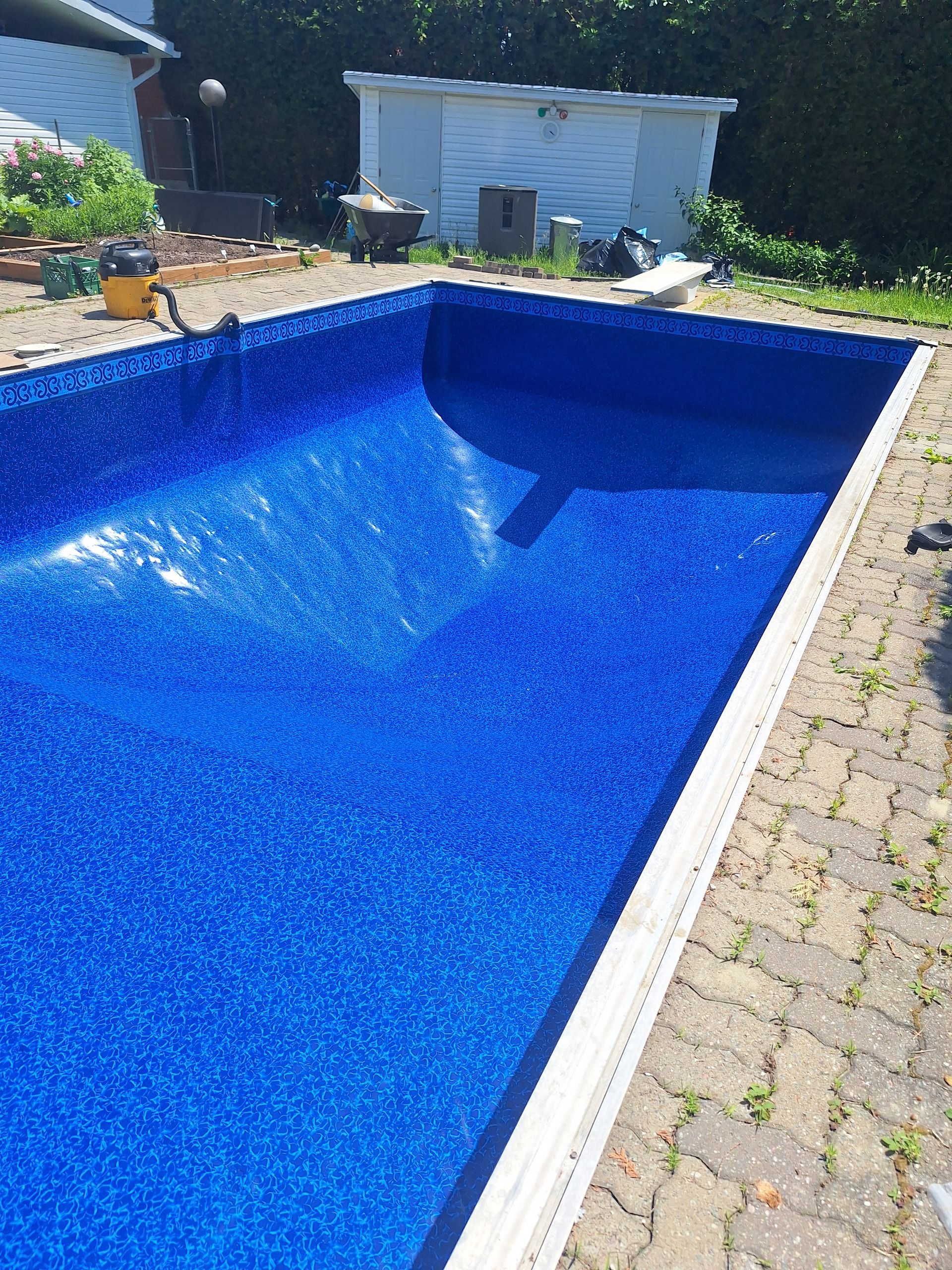 Une piscine rectangulaire avec un revêtement carrelé d'un bleu éclatant, entourée d'une terrasse pavée, située dans un jardin ensoleillé.