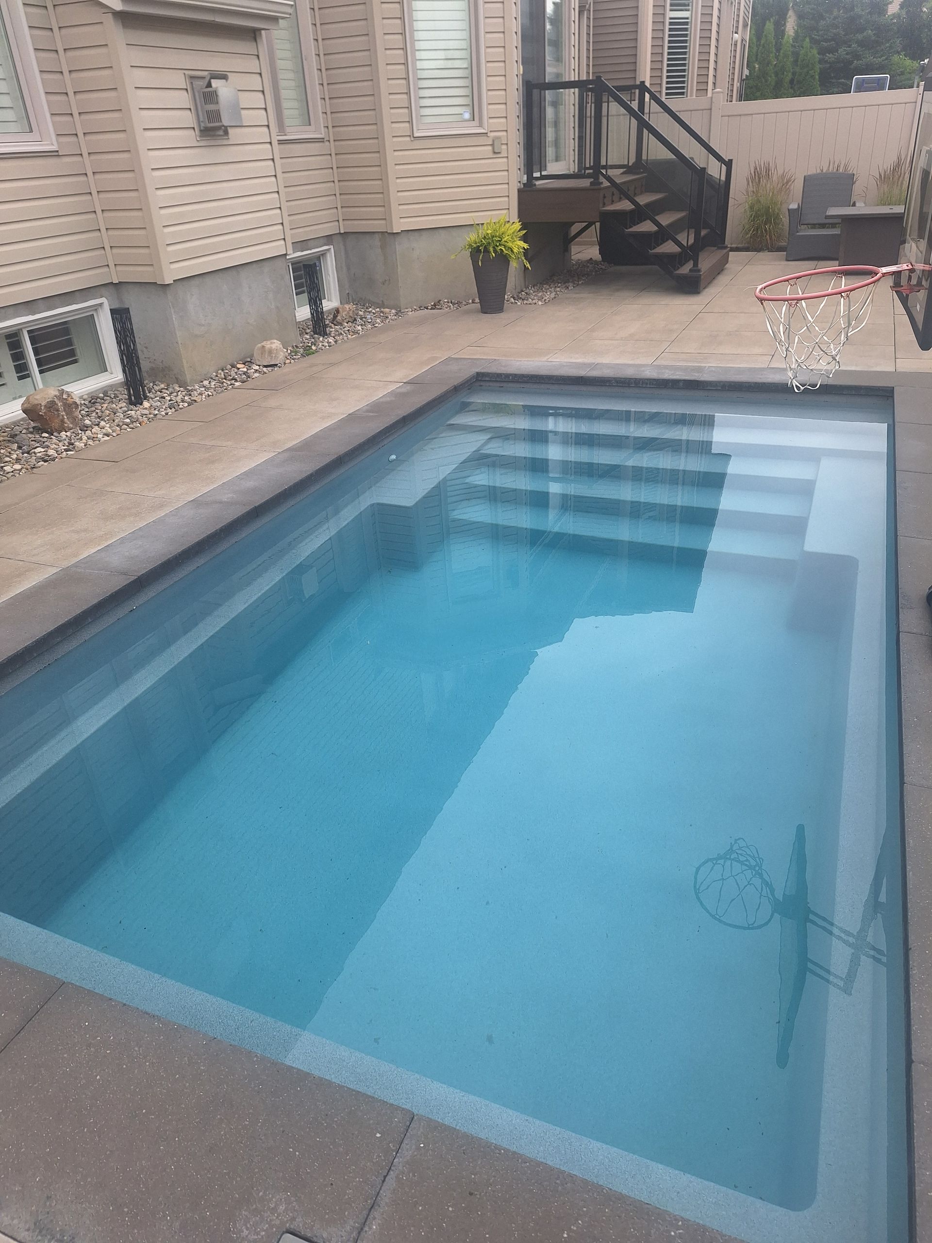 Une piscine rectangulaire à l'eau bleue avec des marches menant à la partie peu profonde, adossée à la terrasse d'une maison.