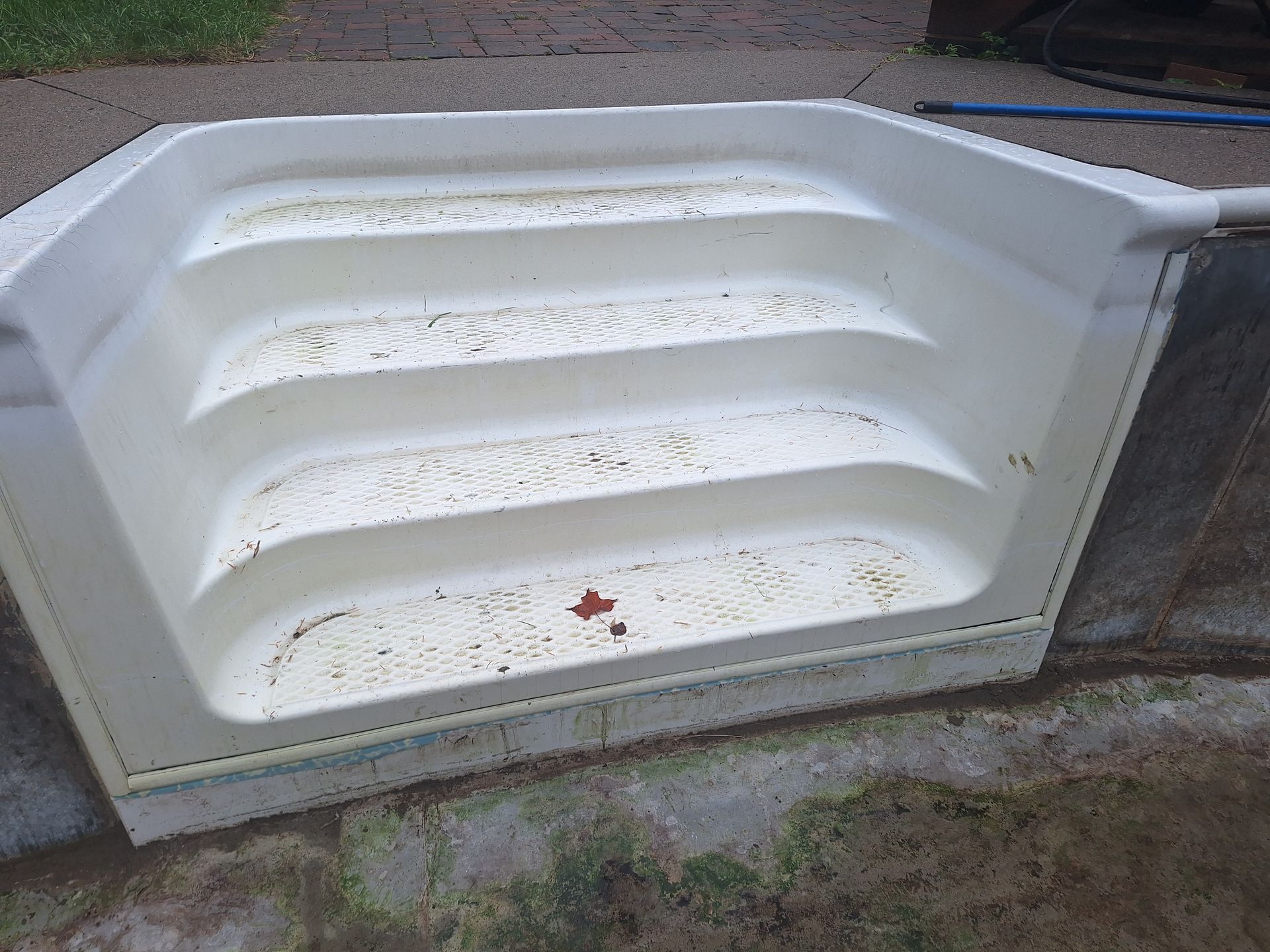 Bloc d'entrée de piscine en plastique moulé blanc à quatre marches, posé sur une terrasse en béton.