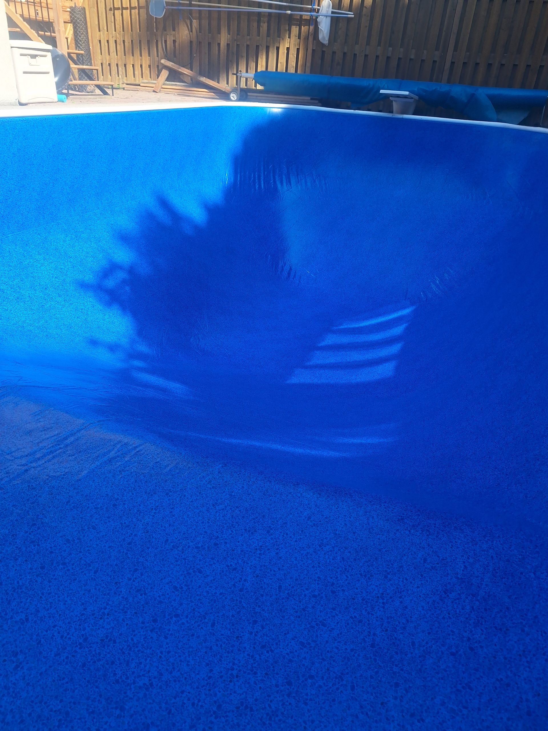 Une bâche de piscine bleu vif, avec des ombres sombres et un reflet rayé projeté sur la paroi.